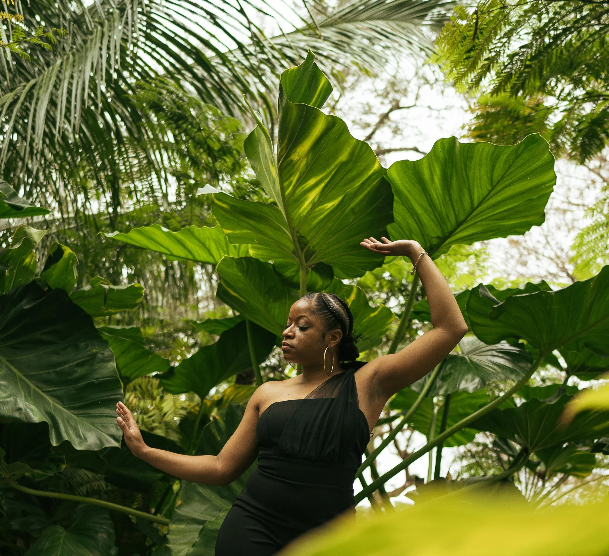 A woman in a black dress poses with large green tropical leaves in a lush outdoor setting in Orlando, Florida.