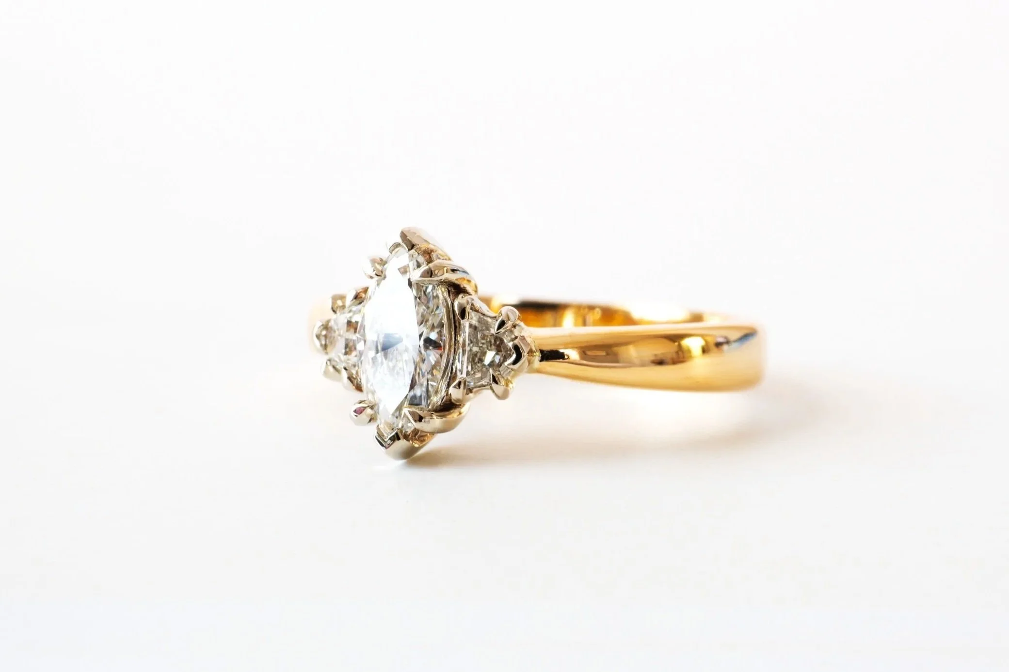 A gold ring featuring a large central diamond surrounded by smaller diamonds, set against a white background.