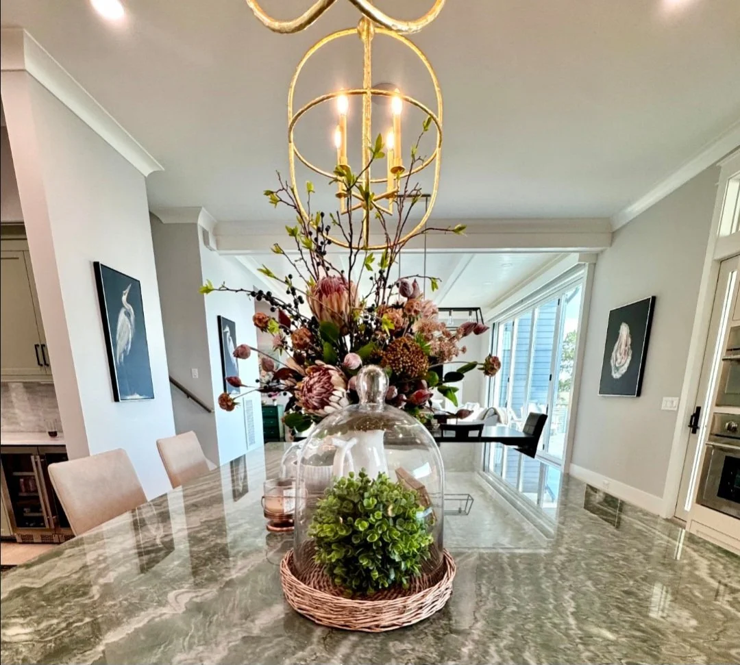 A modern dining room with a marble countertop, decorative floral arrangement in a glass cloche, and a chandelier hanging above.