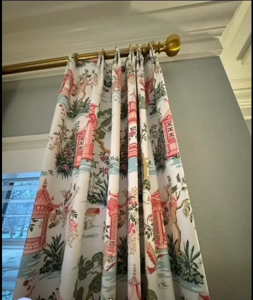 Decorative curtain with Asian-inspired design hanging from a gold curtain rod in a room with light gray walls.