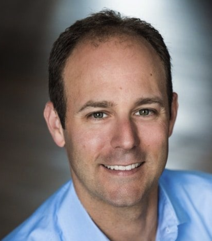Headshot of a man with short brown hair wearing a blue shirt, smiling at the camera.