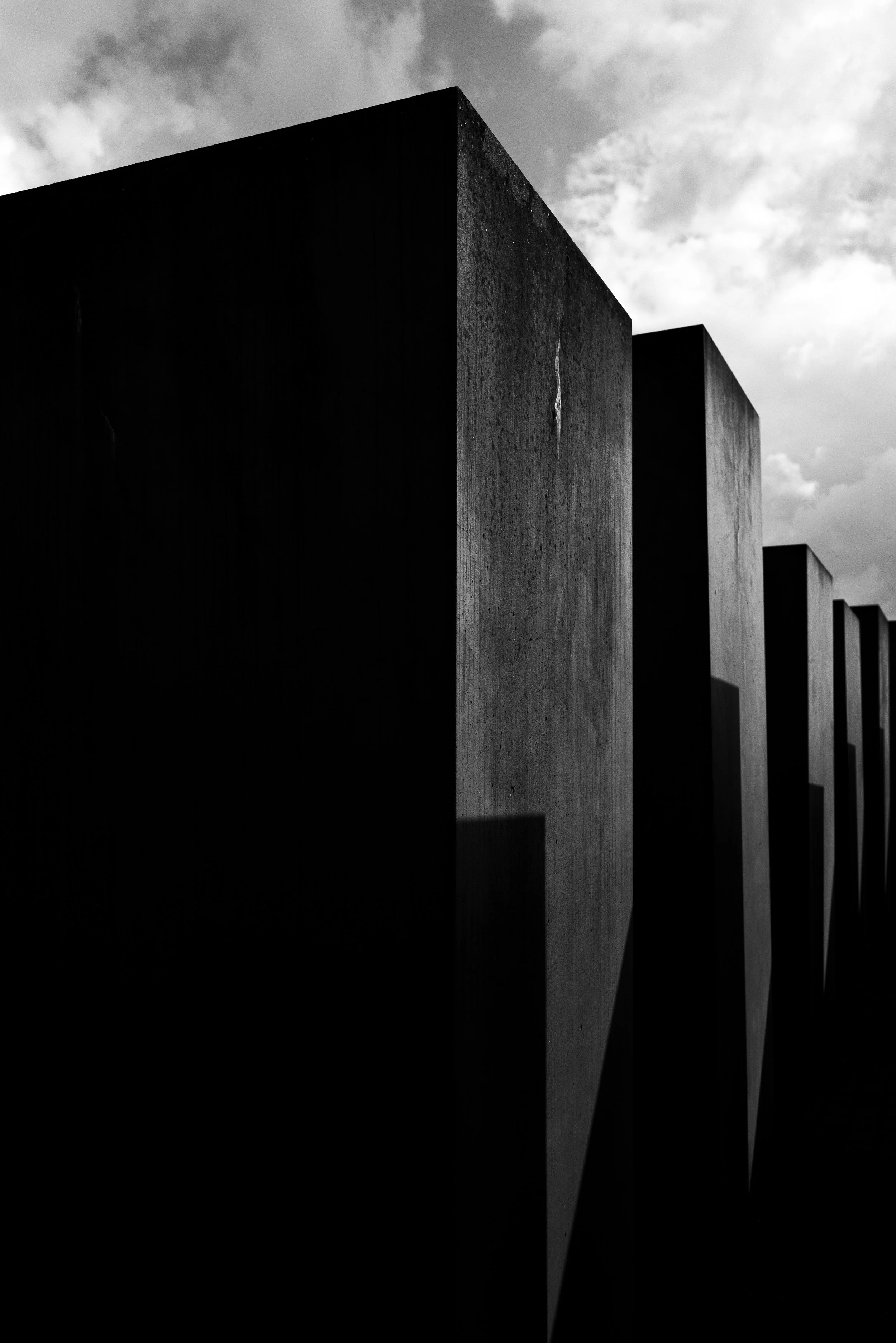 Black and white photo of large rectangular concrete structures with shadows, against a cloudy sky.