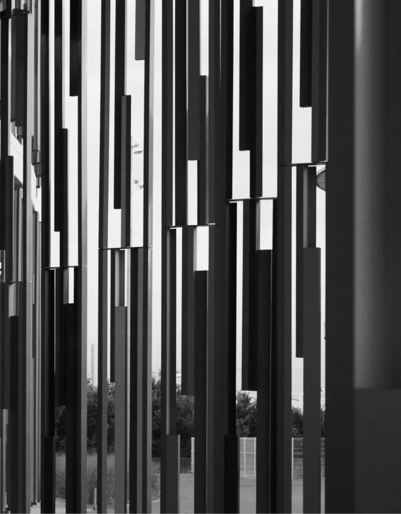 Black and white photo of vertical metal bars with gaps, seen from inside a building, possibly a decorative wall or partition.