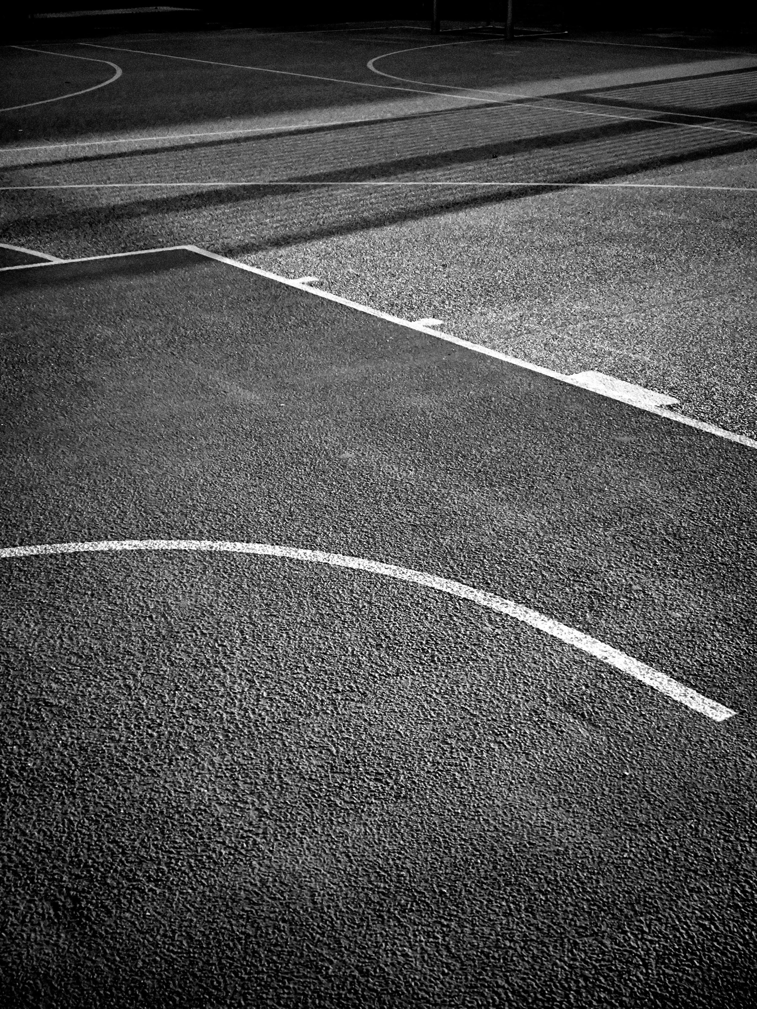 Nighttime view of an empty basketball court with marked court lines, illuminated by lights.
