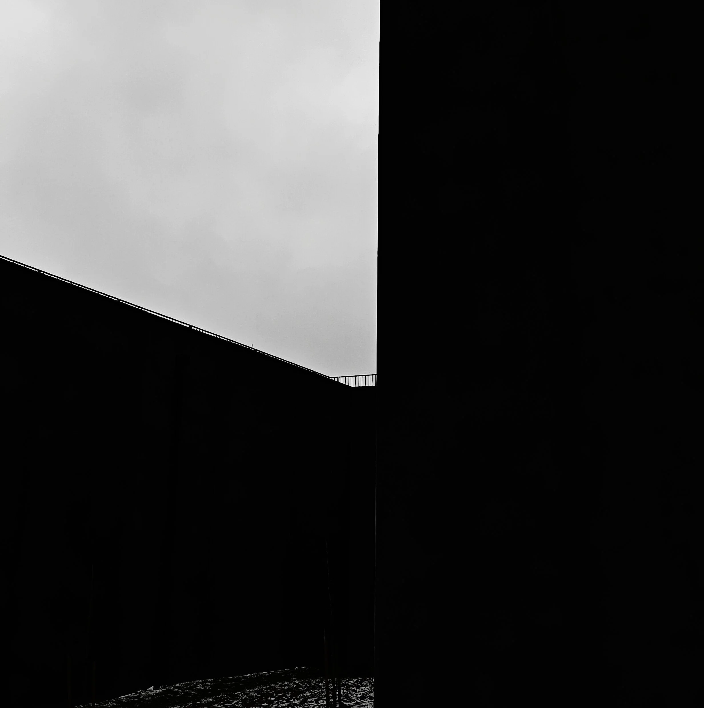 Black building walls with a small opening revealing a cloudy sky.