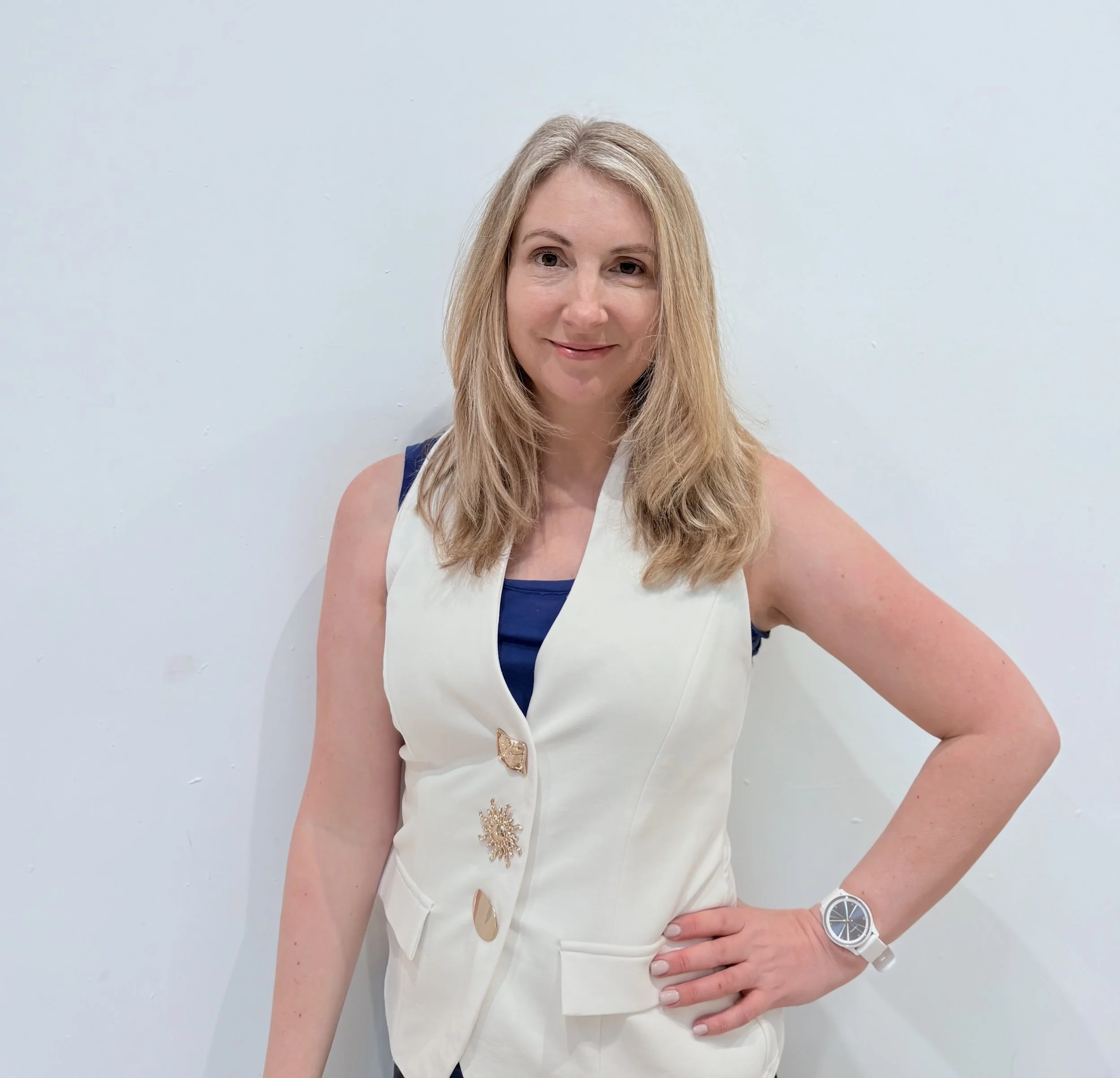 Blonde woman standing against a white background wearing a white waistcoat