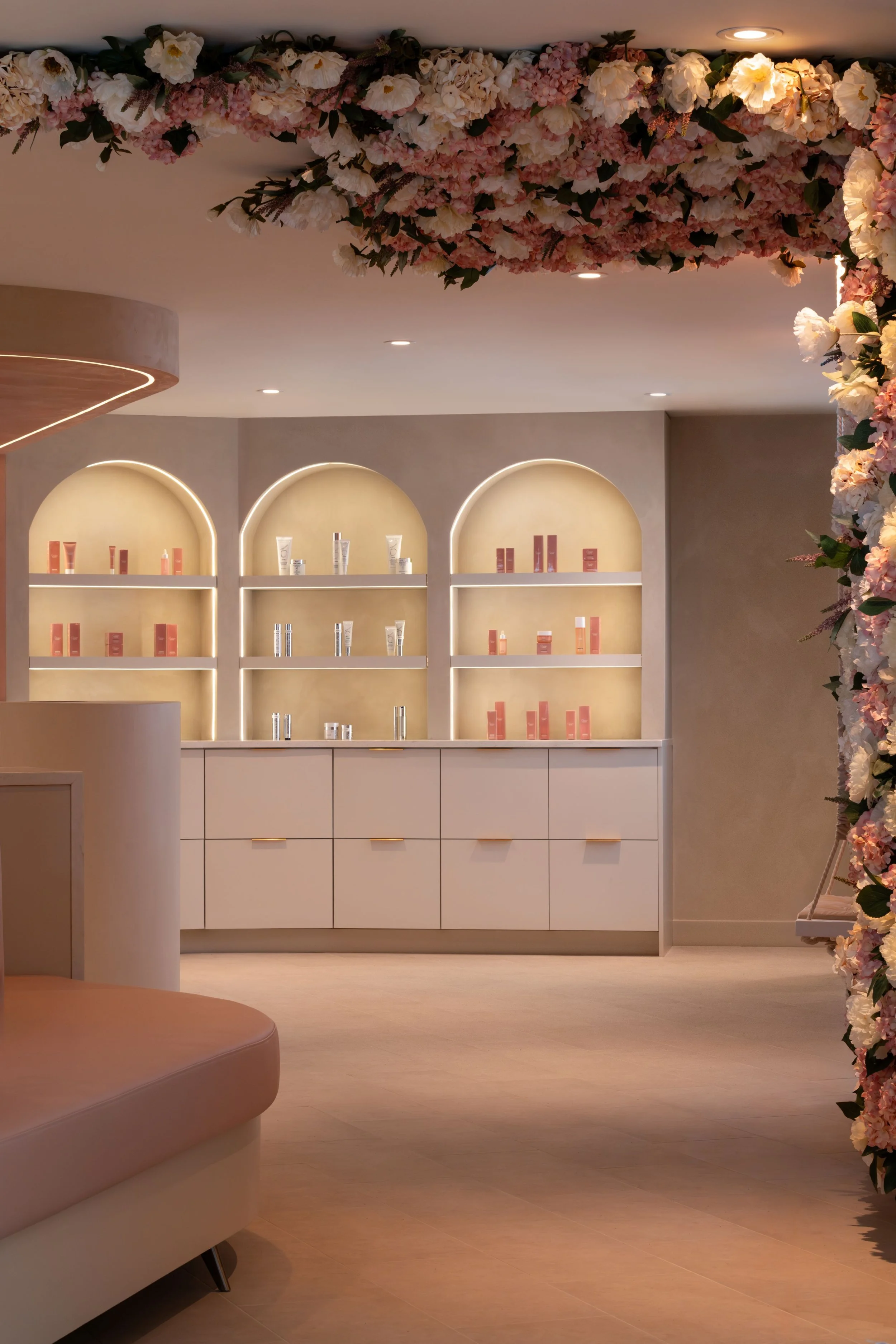 Wellness Interior design of Caviar Skin Clinic., a skin care clinic located in White Rock, British Columbia. Showing arched retail displays retail, flowers on the wall and ceiling, and pink curved custom seating.