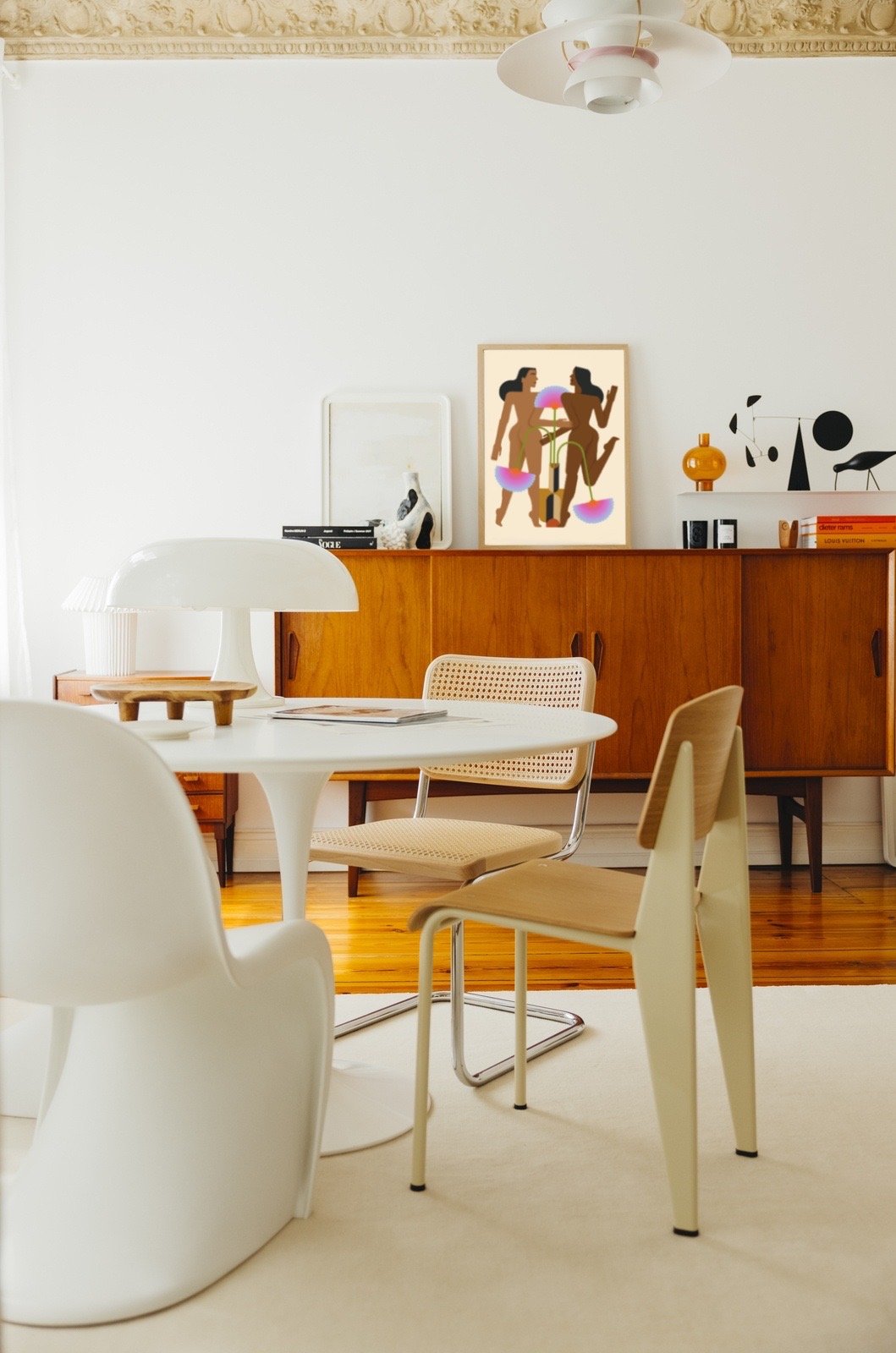Dining room with a white round table, four chairs, and a wooden sideboard with artwork and decorative items on it.