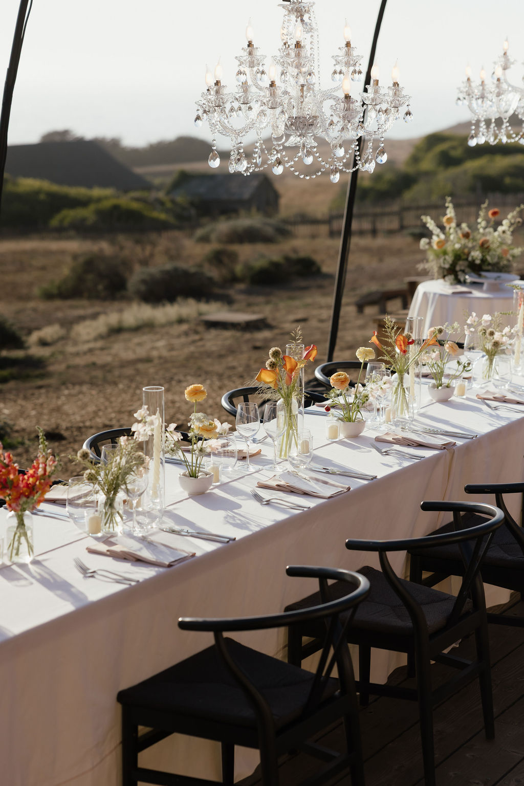 Sunset orange and mustard yellow floral table centerpieces under chandeliers for Sea Ranch wedding reception