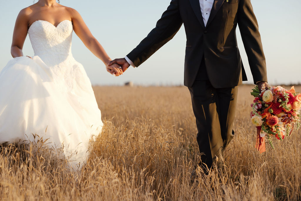 Bride in white gown and groom walking through gold grass field near Sea Ranch ocean cliffs