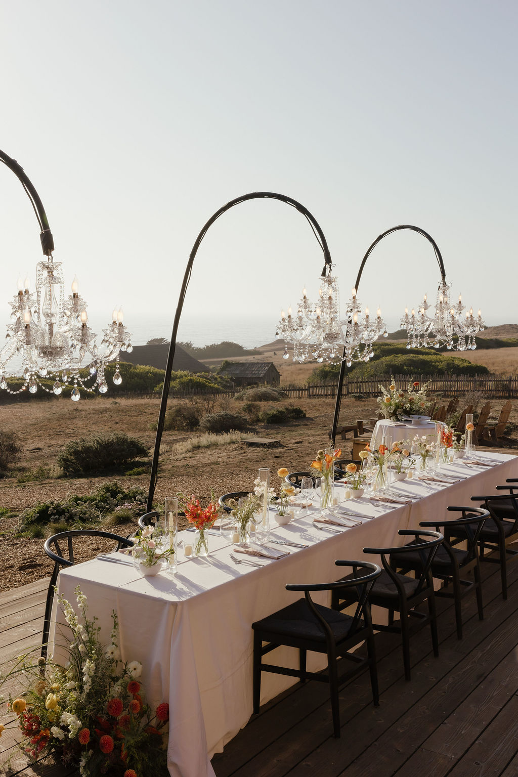 Sunset orange and mustard yellow floral table centerpieces under chandeliers for Sea Ranch wedding reception