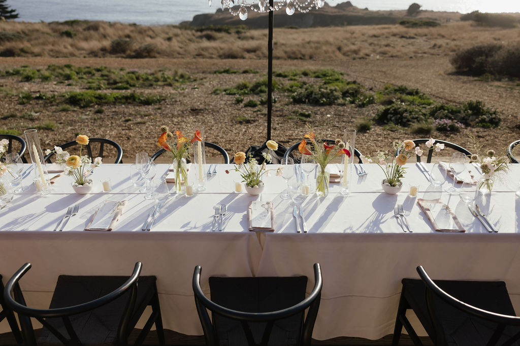 Sunset orange and mustard yellow floral table centerpieces under chandeliers for Sea Ranch wedding reception
