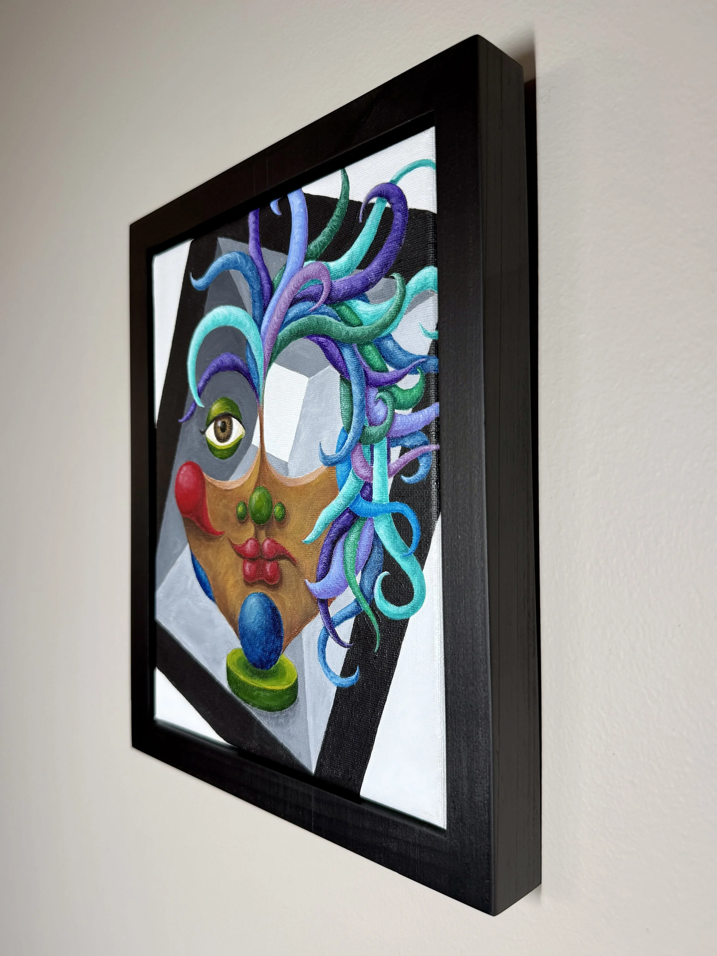Framed artwork of a surreal face with a colorful abstract headdress, painted on canvas.