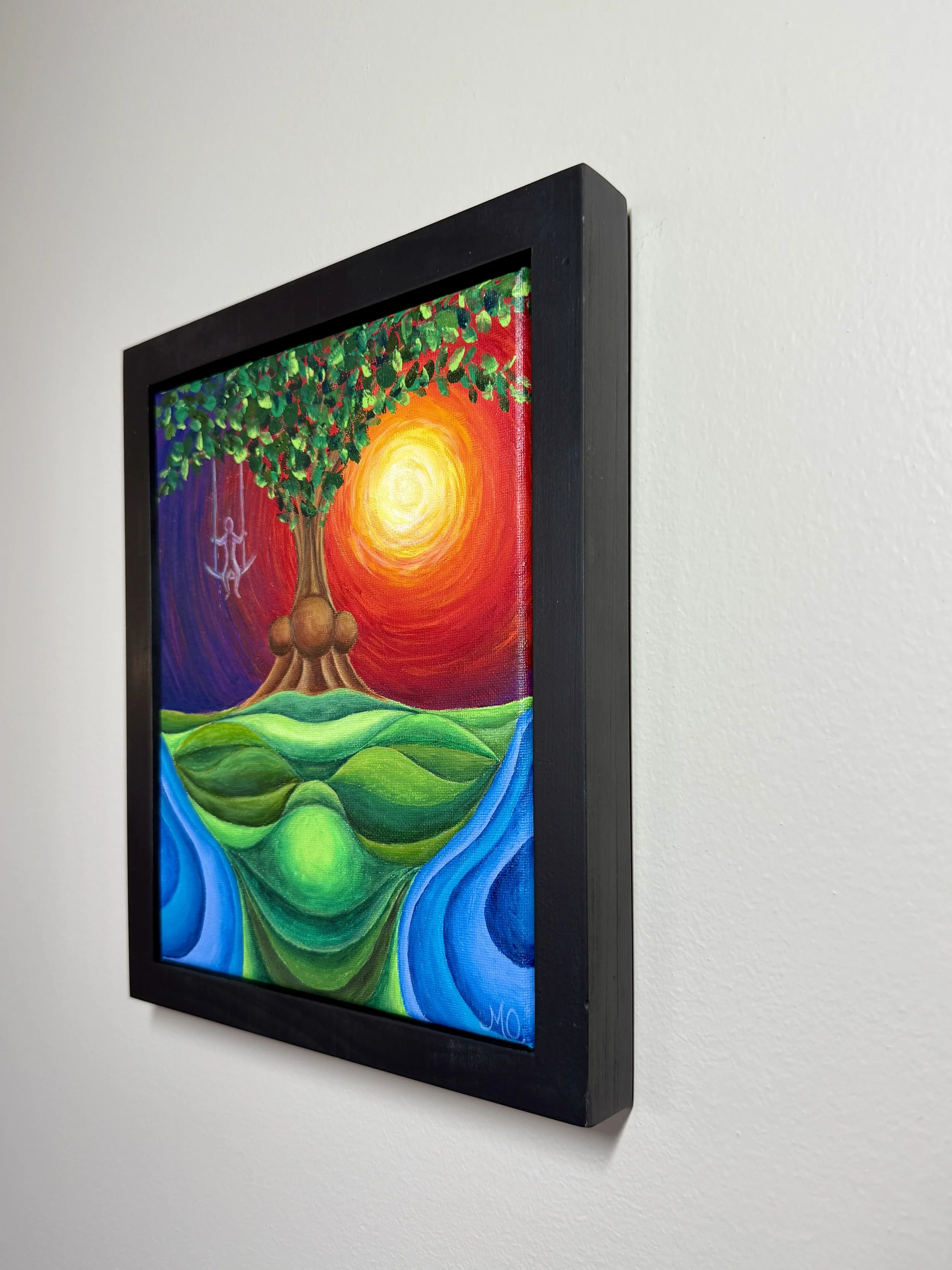 Colorful abstract painting of a tree with a bright yellow sun in the background, framed in black, hanging on a white wall.