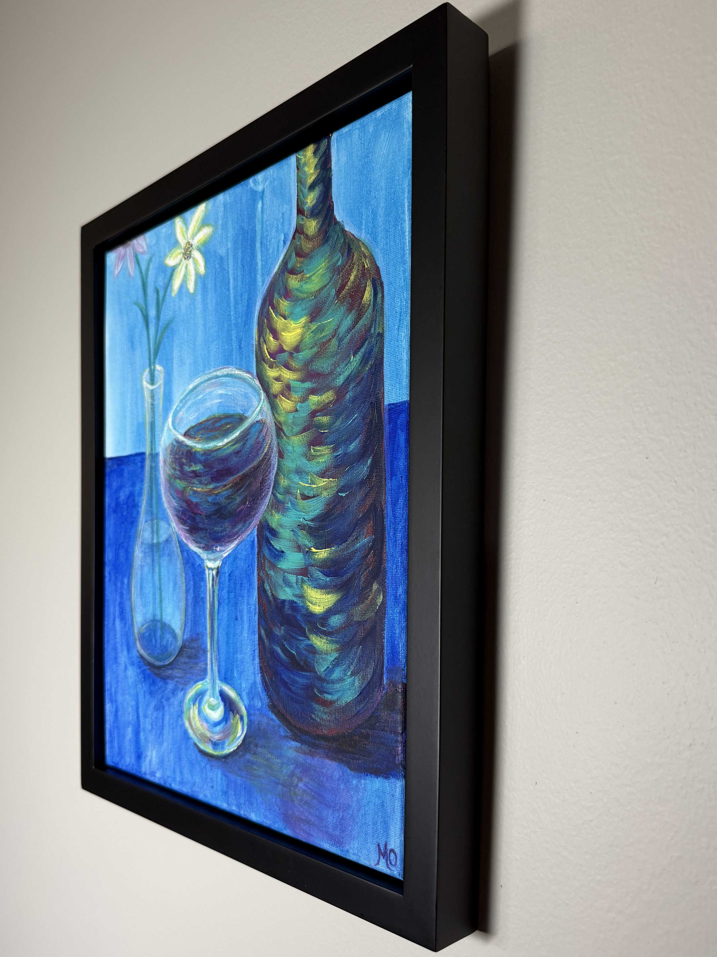Close-up of a colorful oil painting on a black frame wall with a white wall background. The artwork depicts a still life with a vase of flowers, a wine glass, and a tall, multicolored bottle against a blue background.