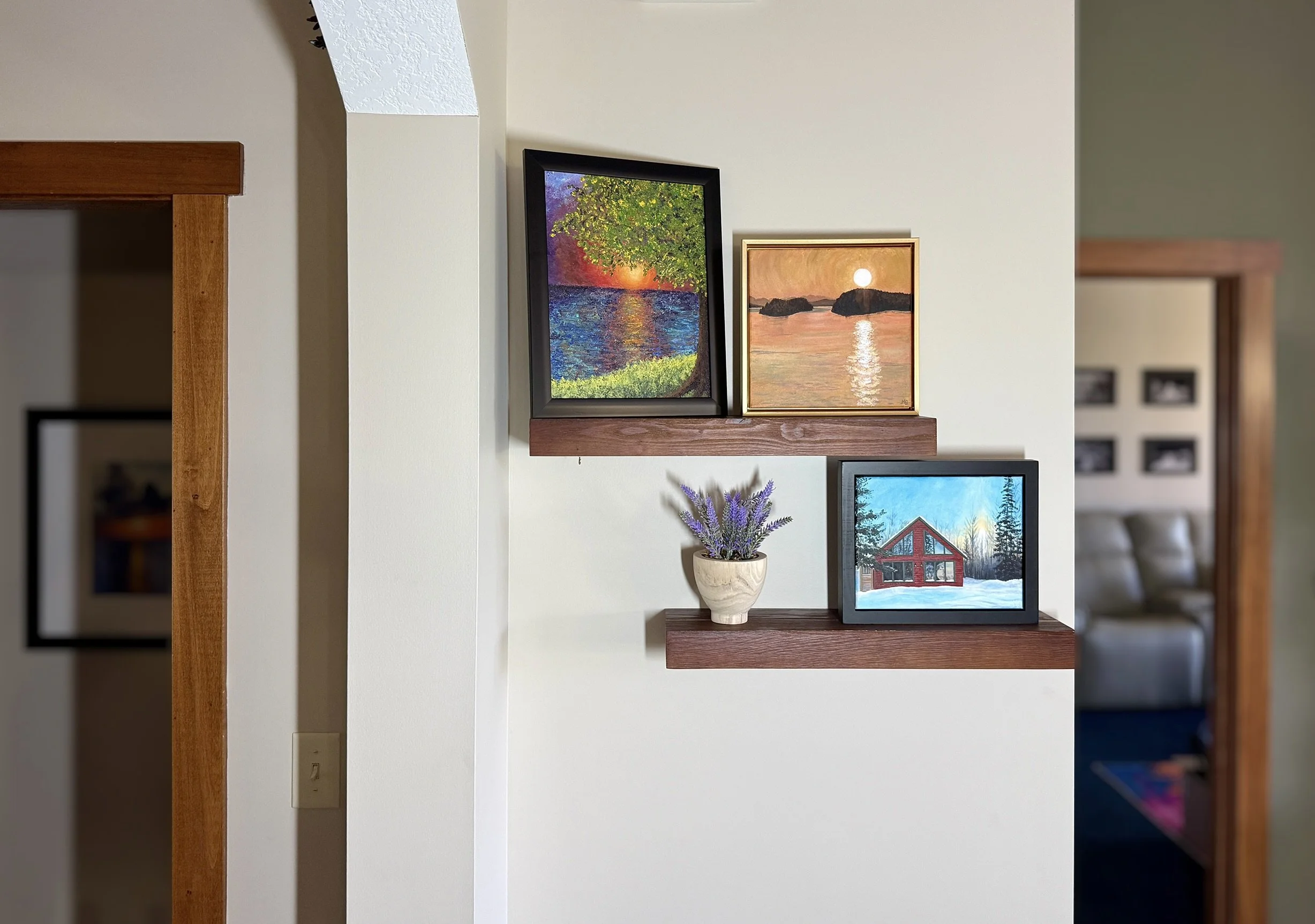 Interior with three framed pictures on wall, a small potted lavender plant on a wooden shelf, and a wooden frame visible on the left.