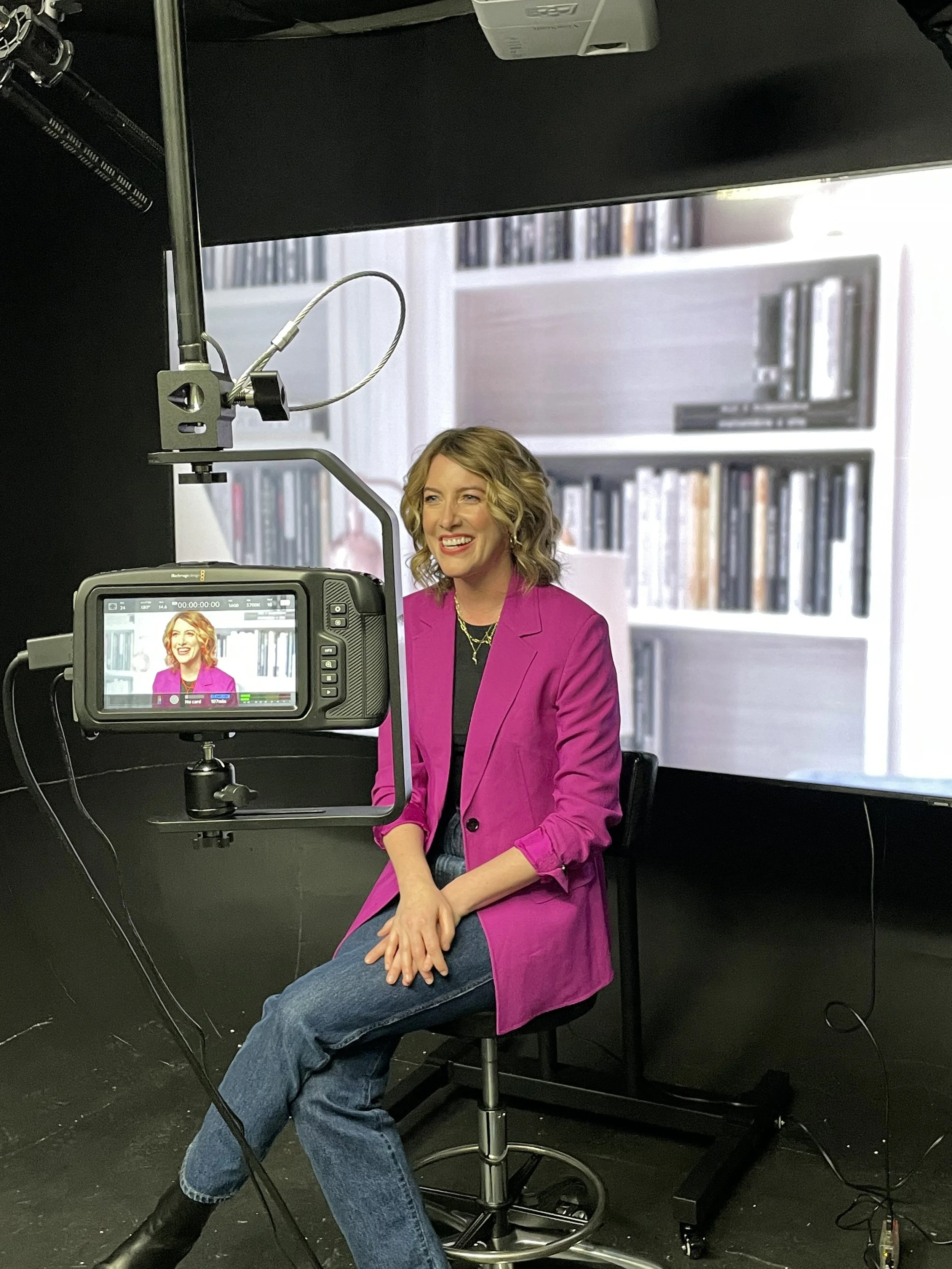 Natalie sits before a camera in a pink blazer
