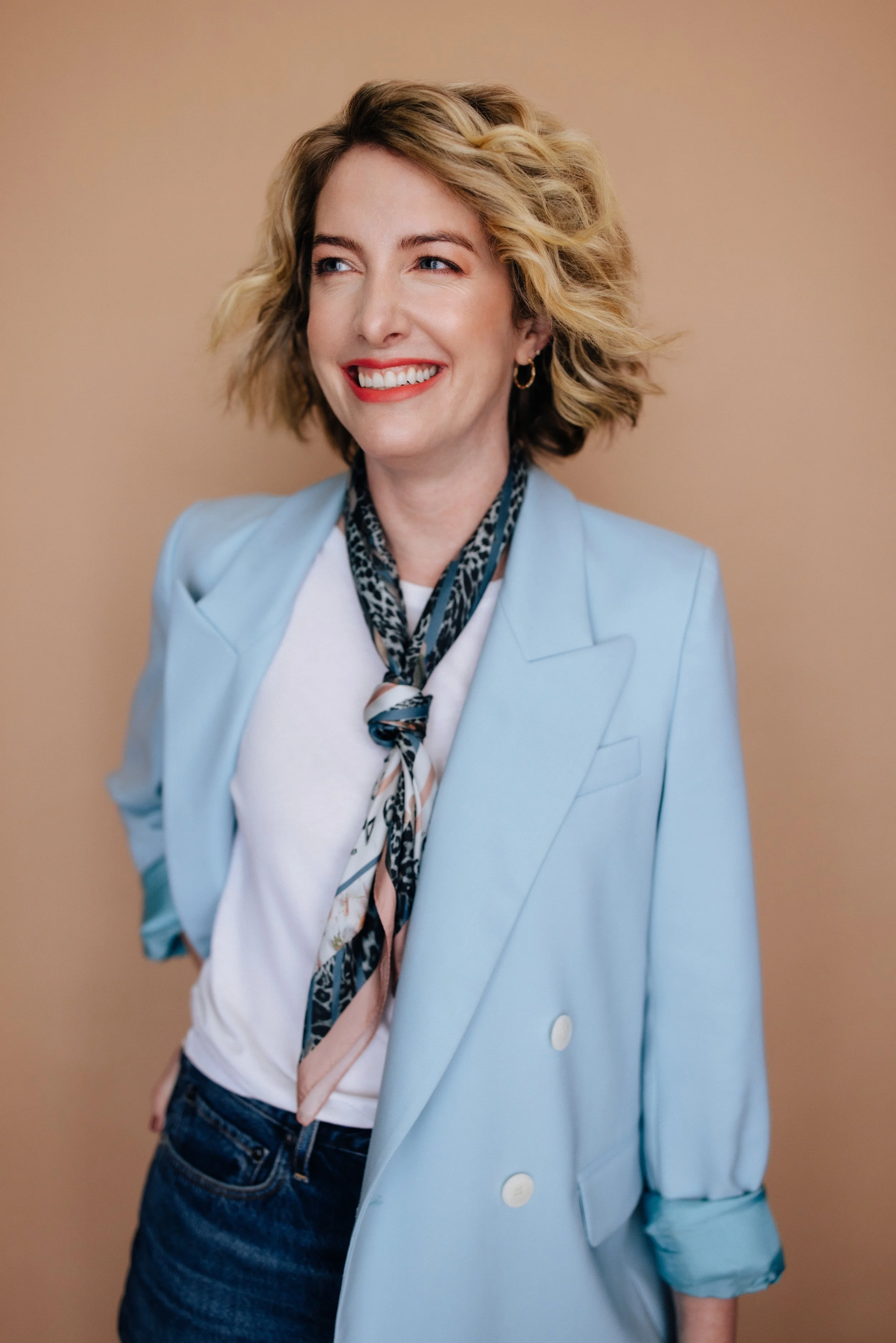 Natalie looks on, wearing an ascot and a baby blue blazer