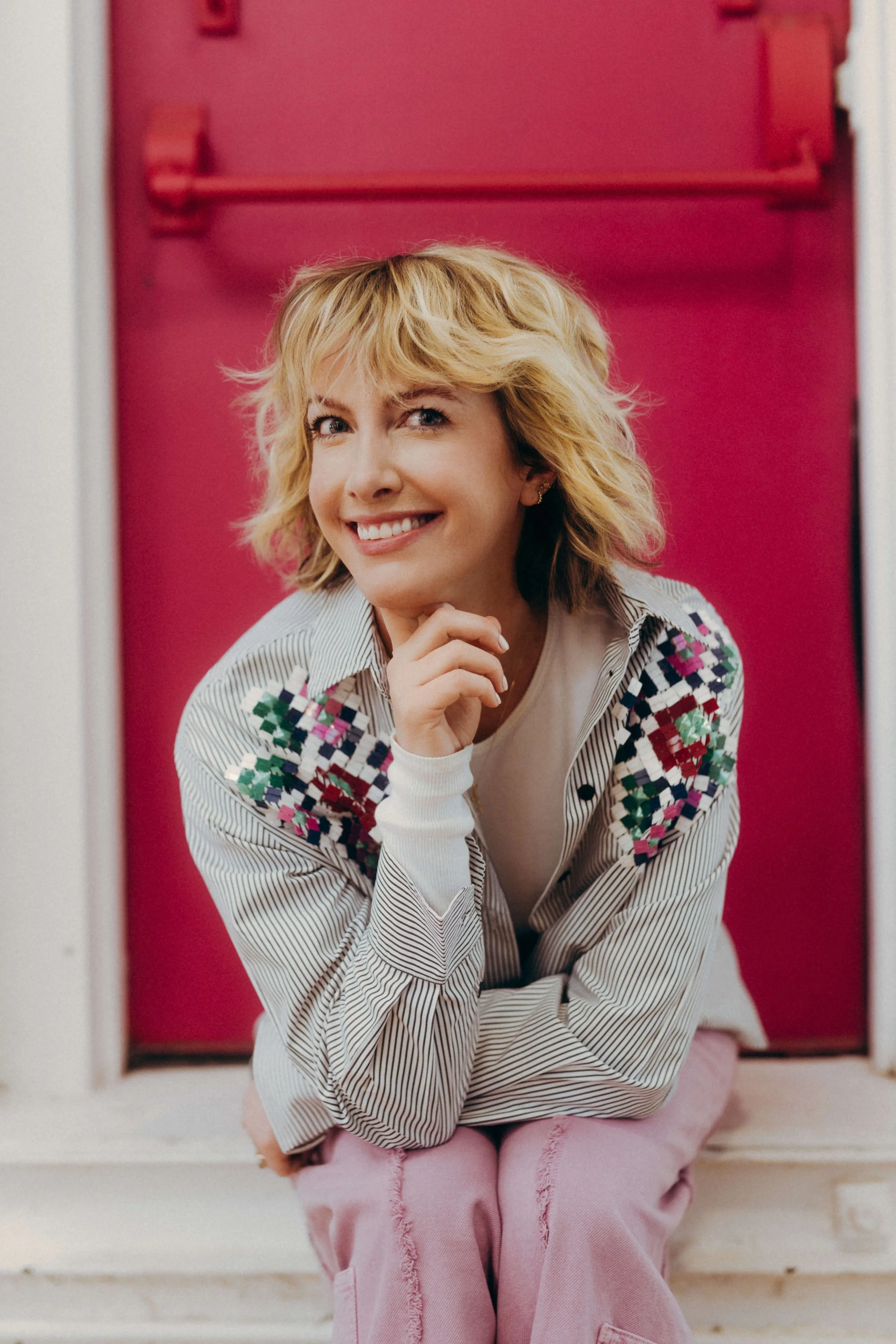 Natalie sits before a magenta door, holding her chin