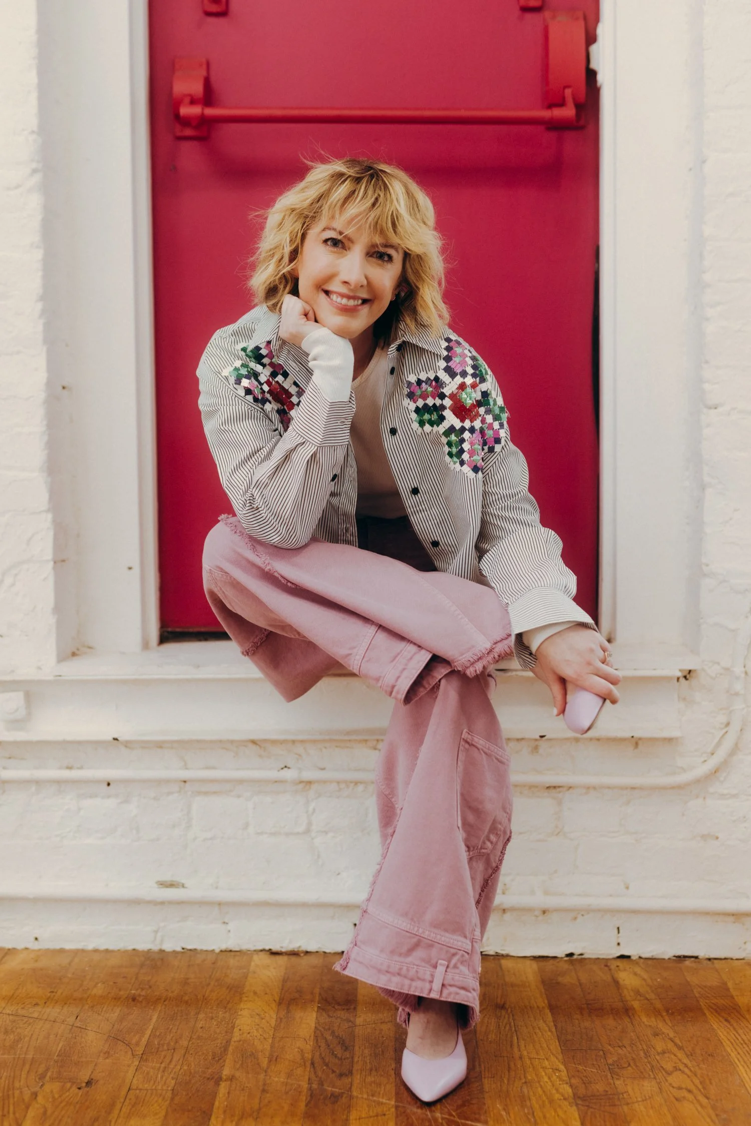 Natalie sits with legs crossed before a magenta door