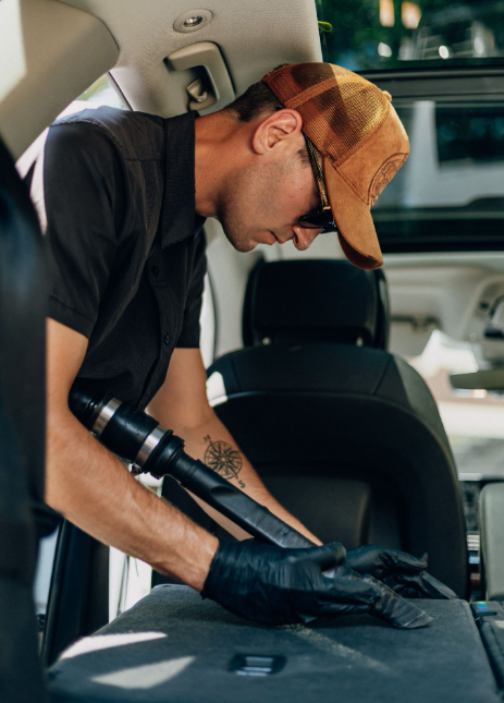 The photo shows the lead detailer vacuuming the upholstery of rear vehicle seats.