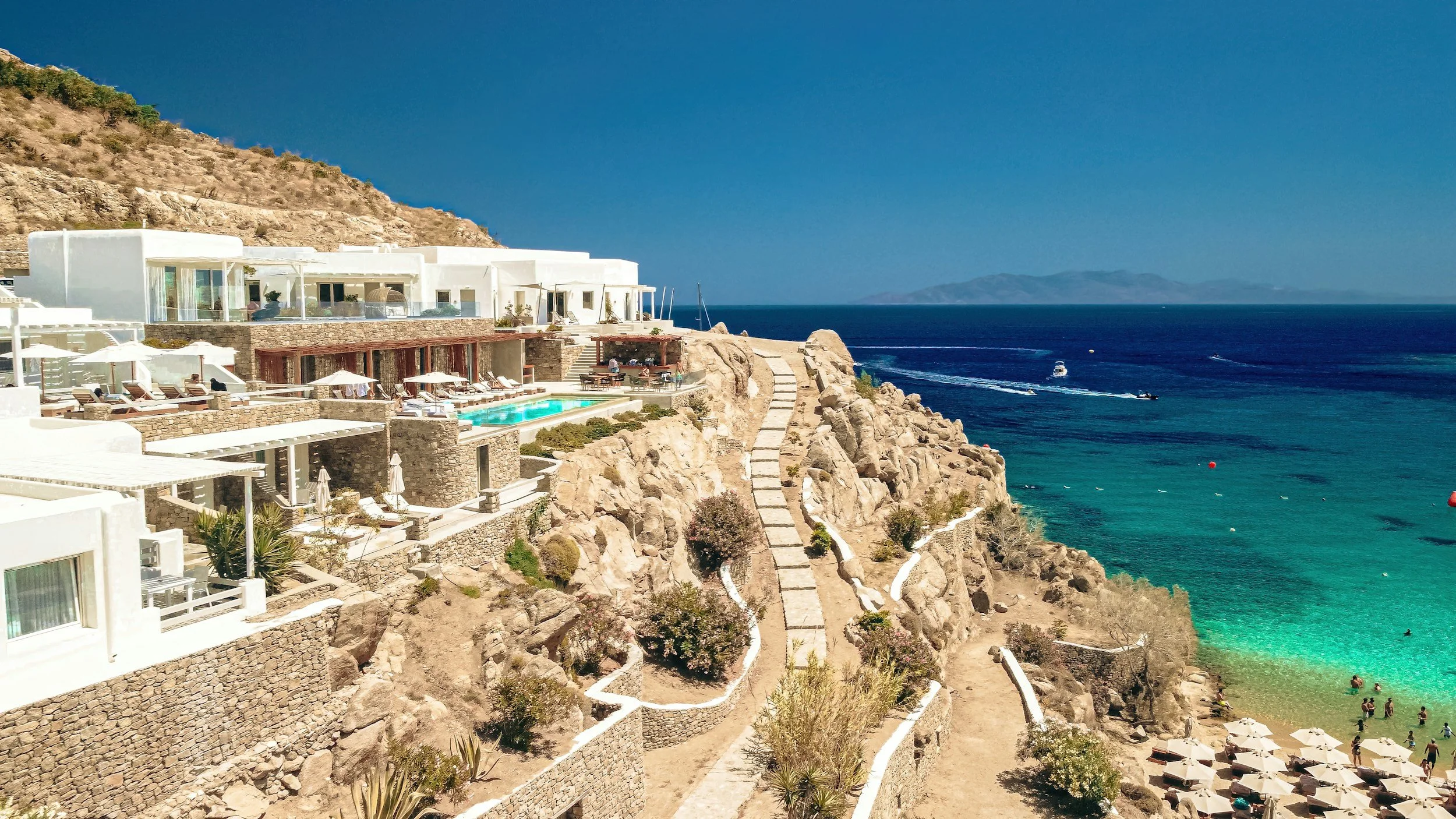 Luxury boutique hotel in Agios Nikolaos, Crete, built along a rocky cliff with infinity pools and views of the turquoise Aegean Sea. Showcasing why September in Crete offers affordable luxury, fewer crowds, and breathtaking seaside stays