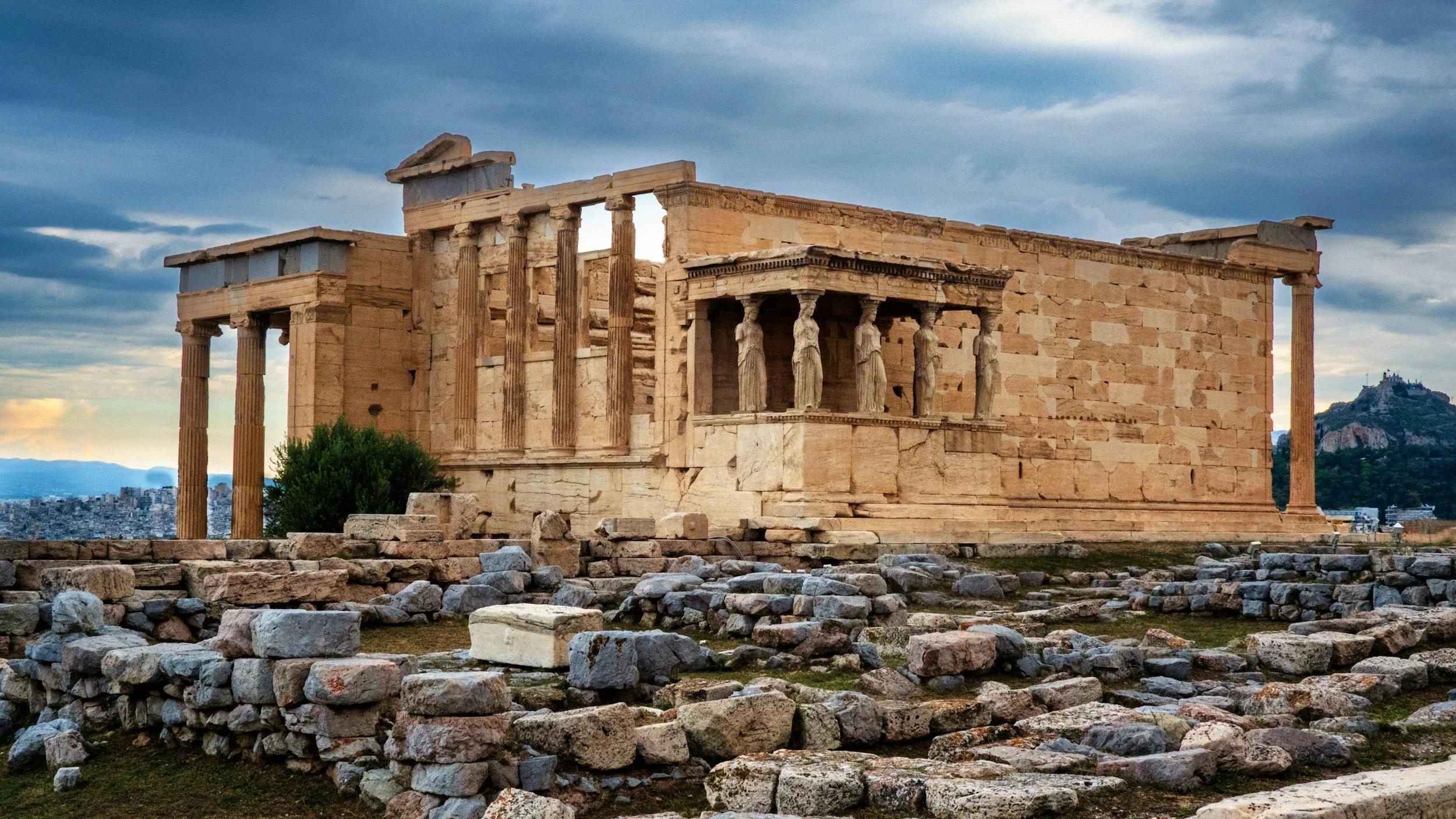 View of the Erechtheion temple on the Acropolis of Athens, Greece, with its ancient stone columns and cloudy autumn sky — a landmark tied to the myth of Athena and Poseidon