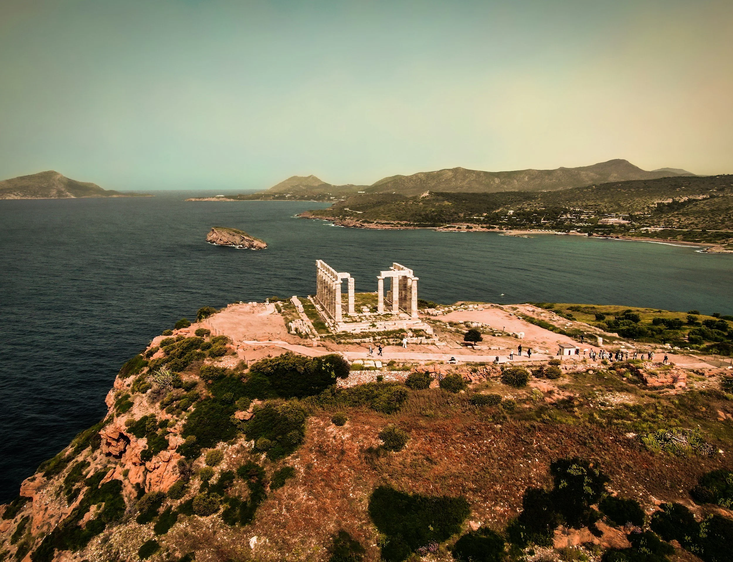 Aerial view of the Temple of Poseidon at Cape Sounion, Greece, perched on a rocky cliff overlooking the Aegean Sea — a mythological site famous for sunsets and the legend of King Aegeus.