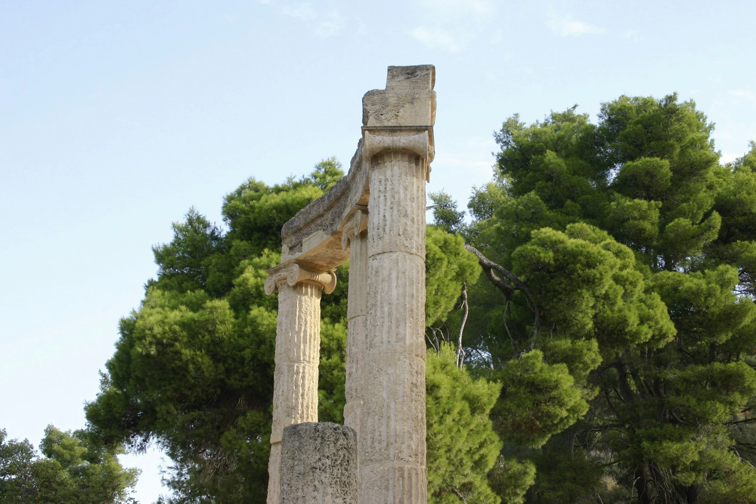 Ancient stone columns at the citadel of Mycenae in Greece, surrounded by green trees — legendary home of Agamemnon and a key site in Greek mythology and the Trojan War.