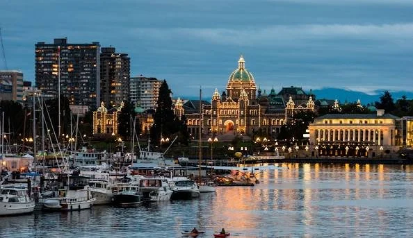 A city skyline with a historic building featuring a green dome, high-rise buildings, and a harbor with boats at dusk.