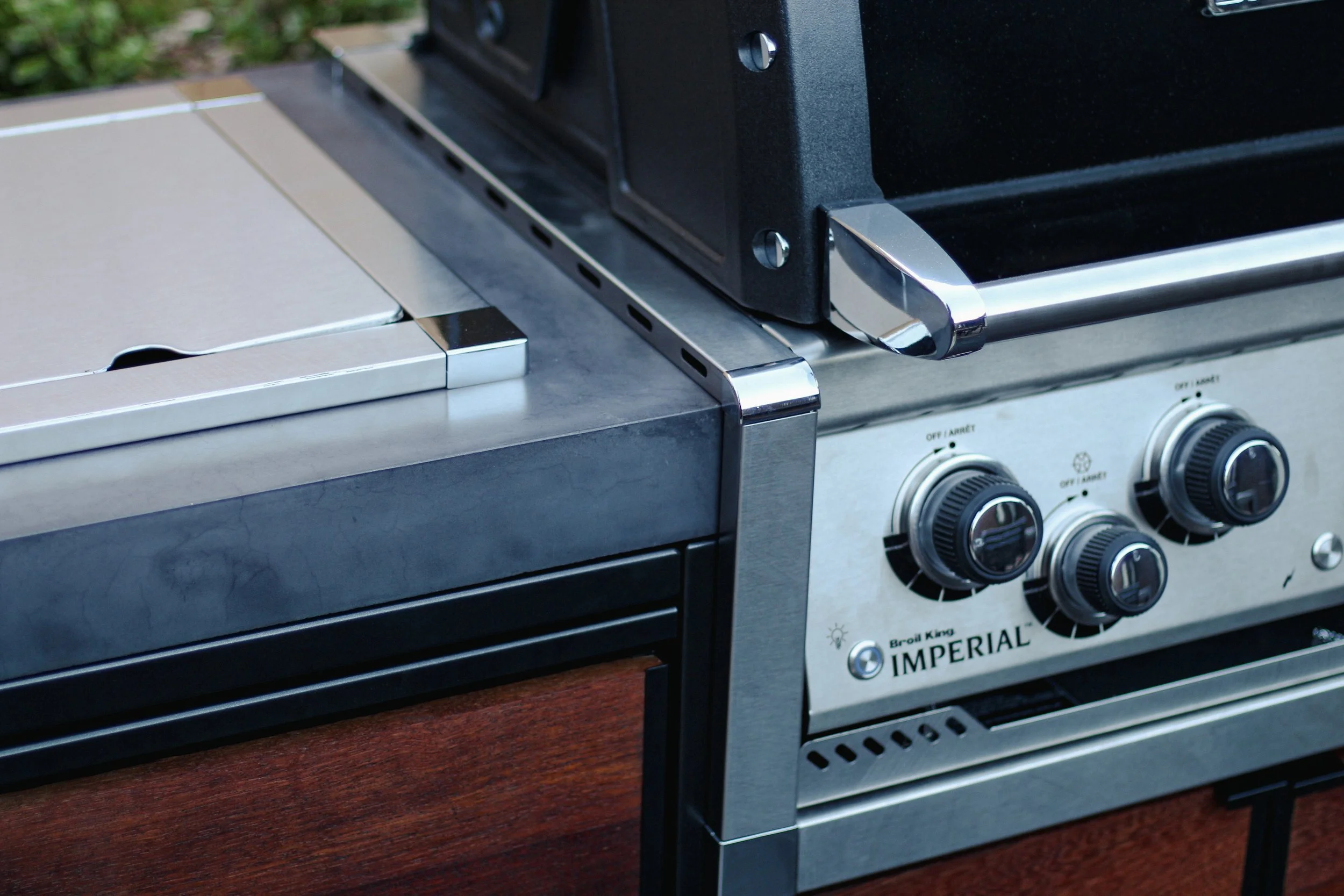 A stainless steel outdoor gas grill with black control knobs and wooden side panels.