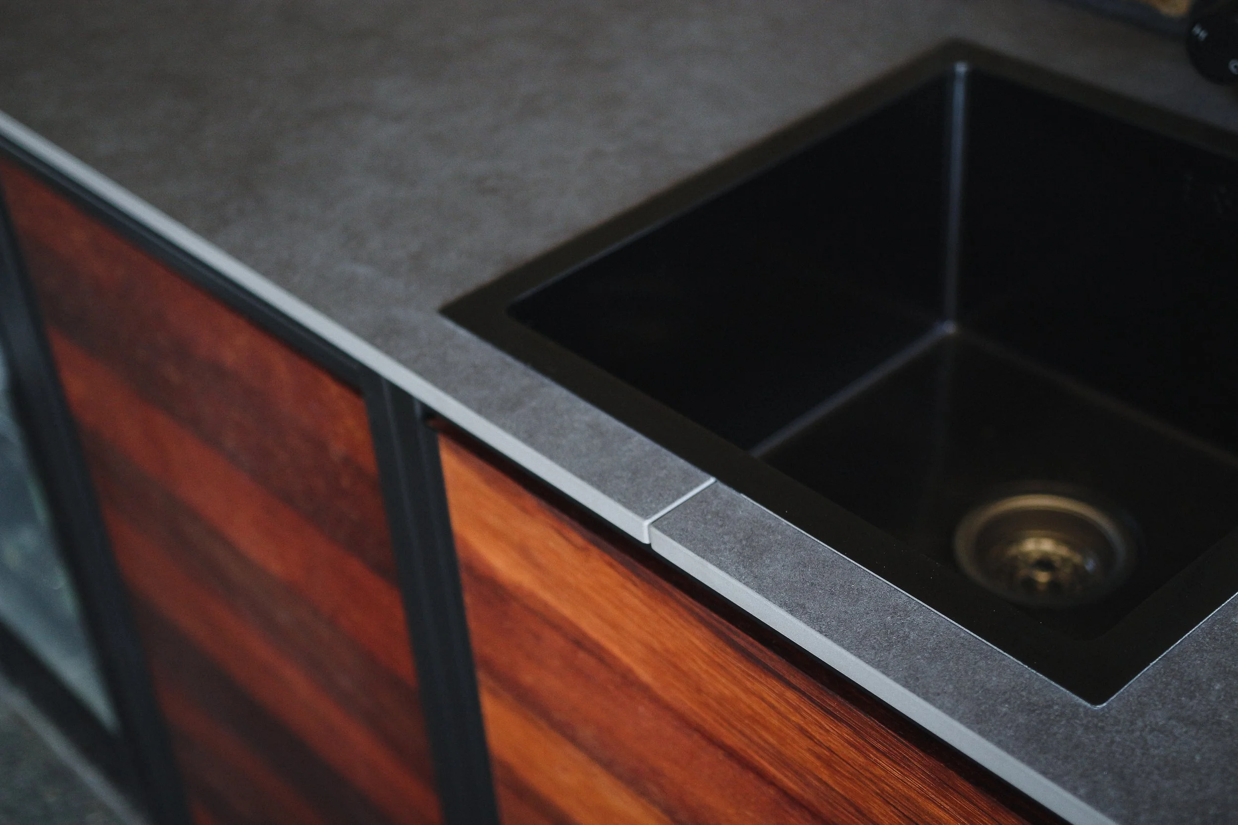 A black kitchen sink installed in a gray countertop with a wooden cabinet below.
