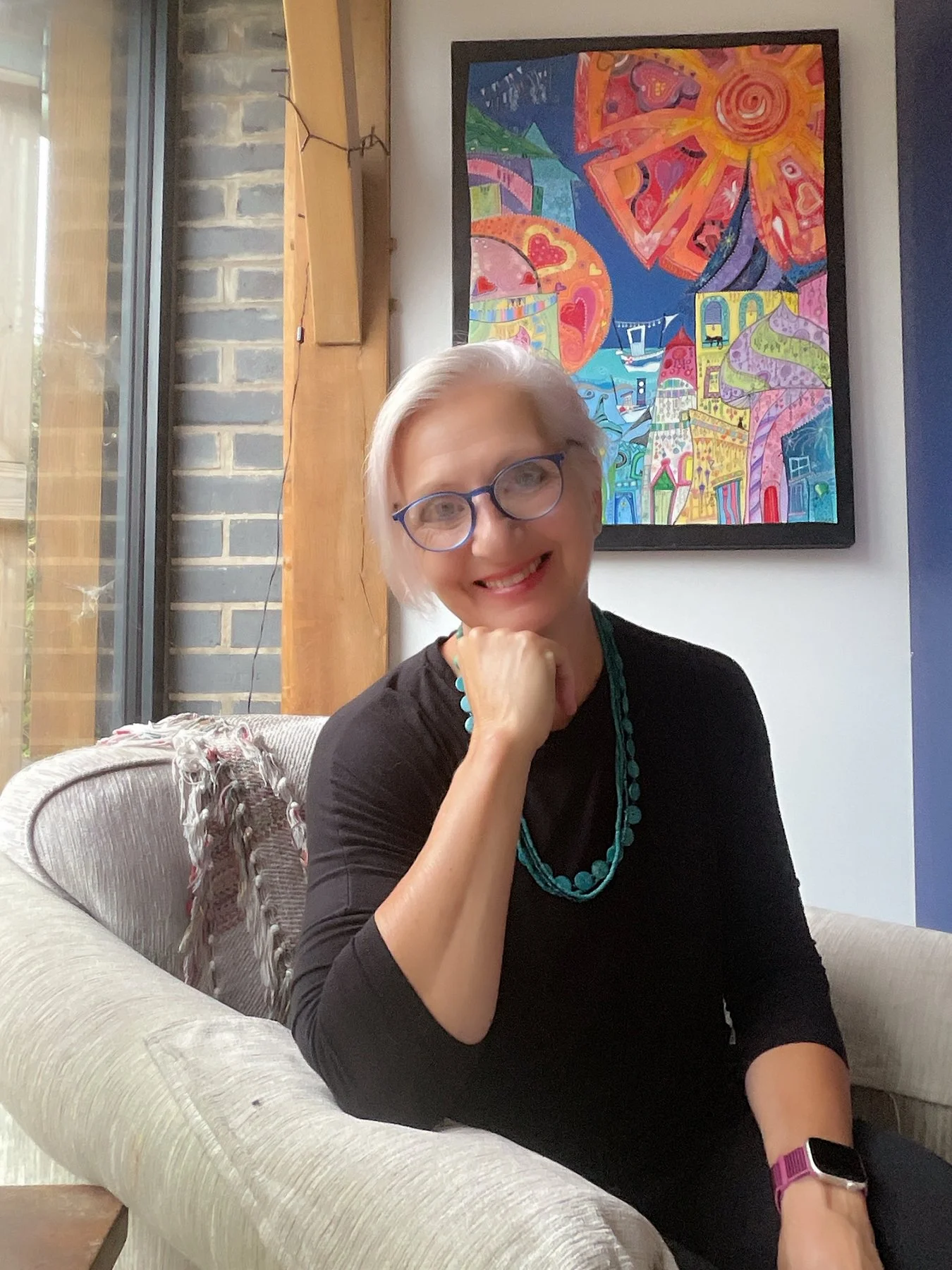 Artist and teacher Cate Field seated in her Dorset home with her colourful Sunshine Festival painting