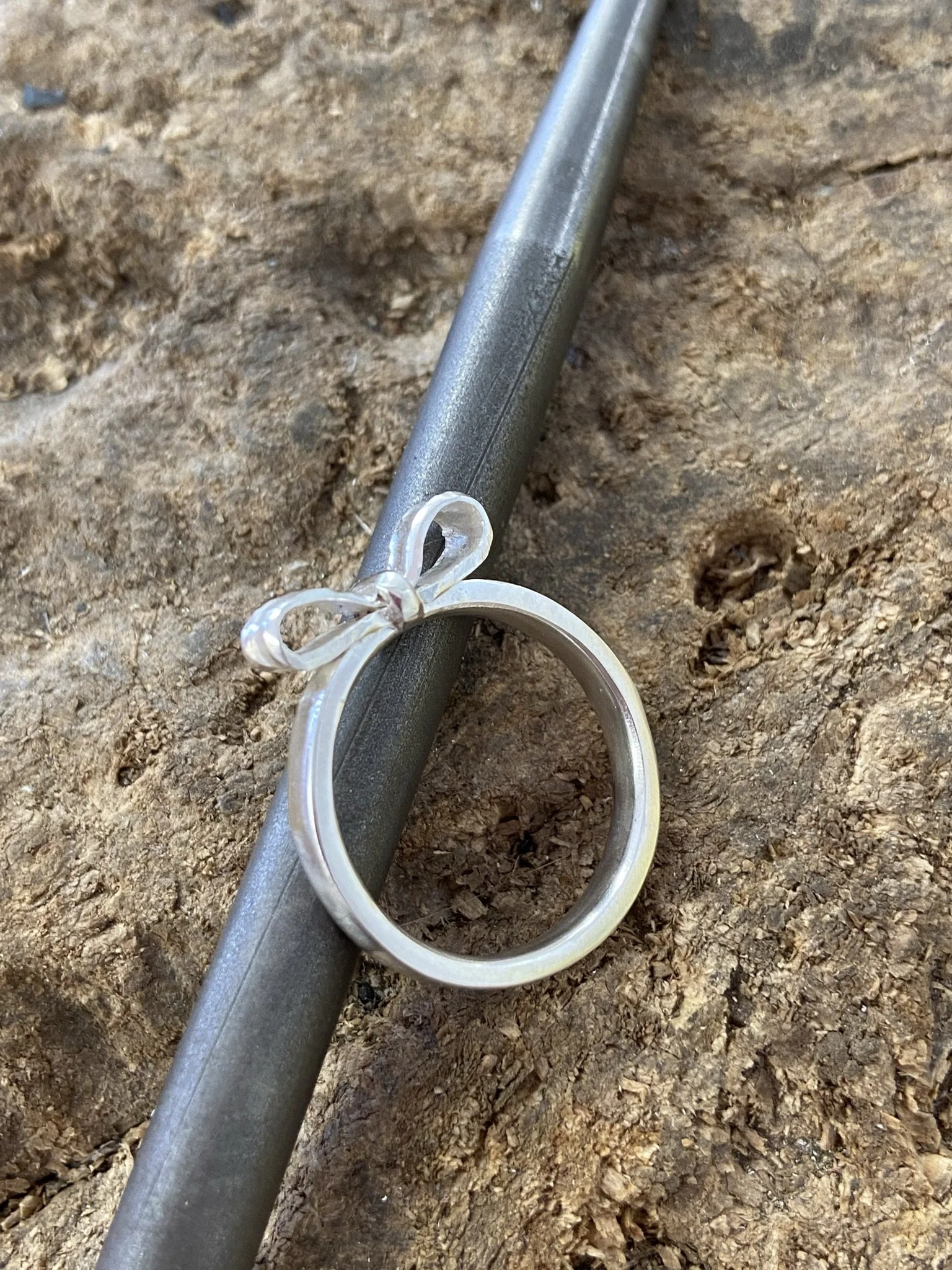 Bow Ring in silver sitting on wooden stump