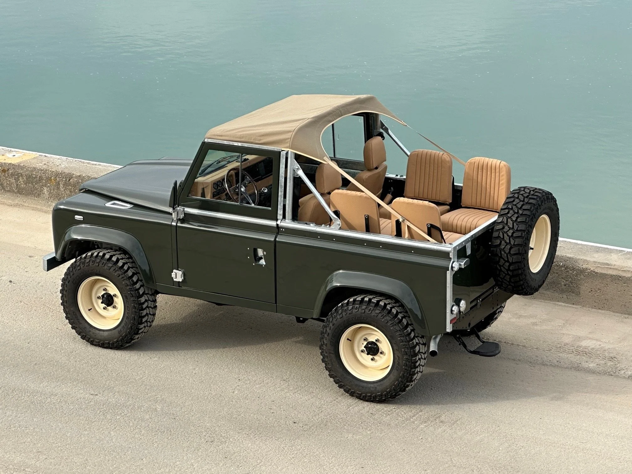 A vintage off-road vehicle with a beige canopy and tan interior seats parked beside a body of water.