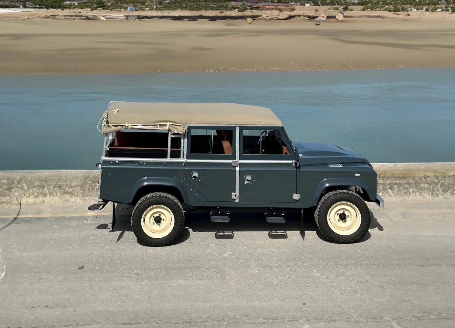 A vintage off-road vehicle parked on a beach near water.