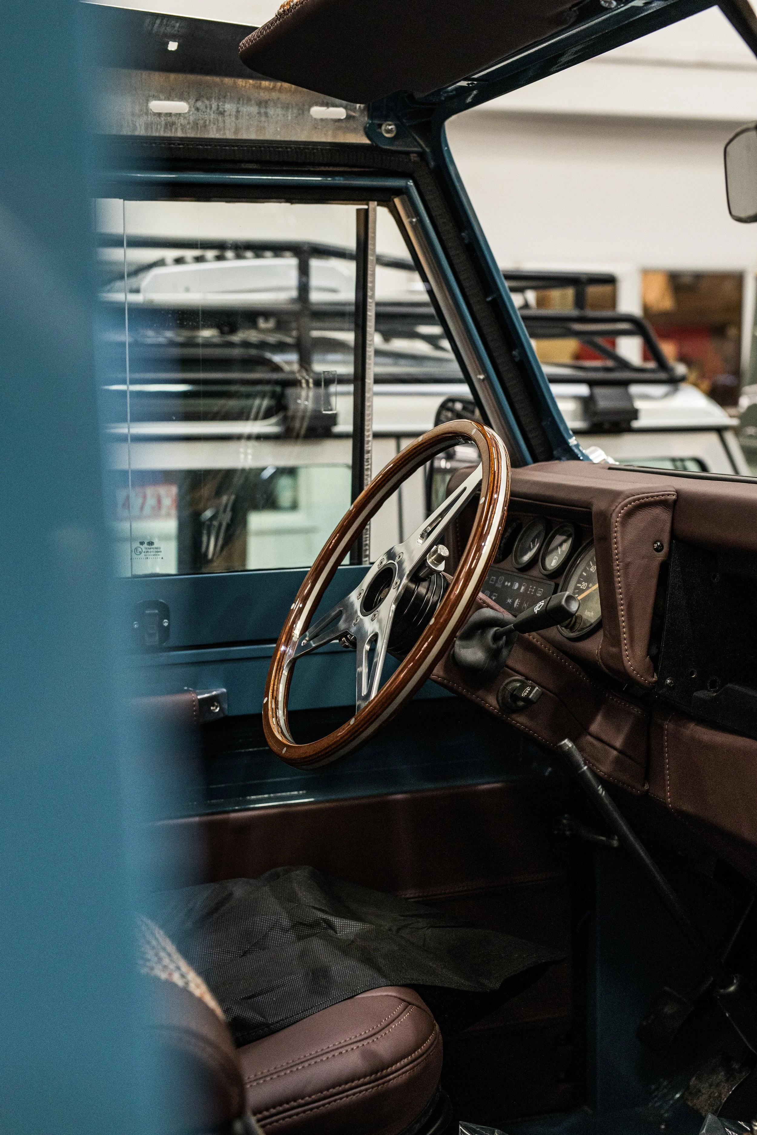 Close-up view of the interior of a vintage vehicle, showing a wooden steering wheel, dashboard with gauges, brown leather upholstery, and a gear shift lever.