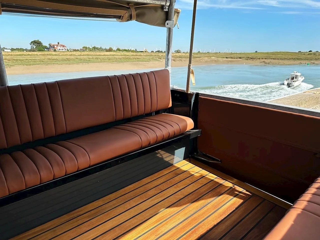 View from a boat's deck with brown leather seating, overlooking water and a small motorboat pulling away on a sunny day.