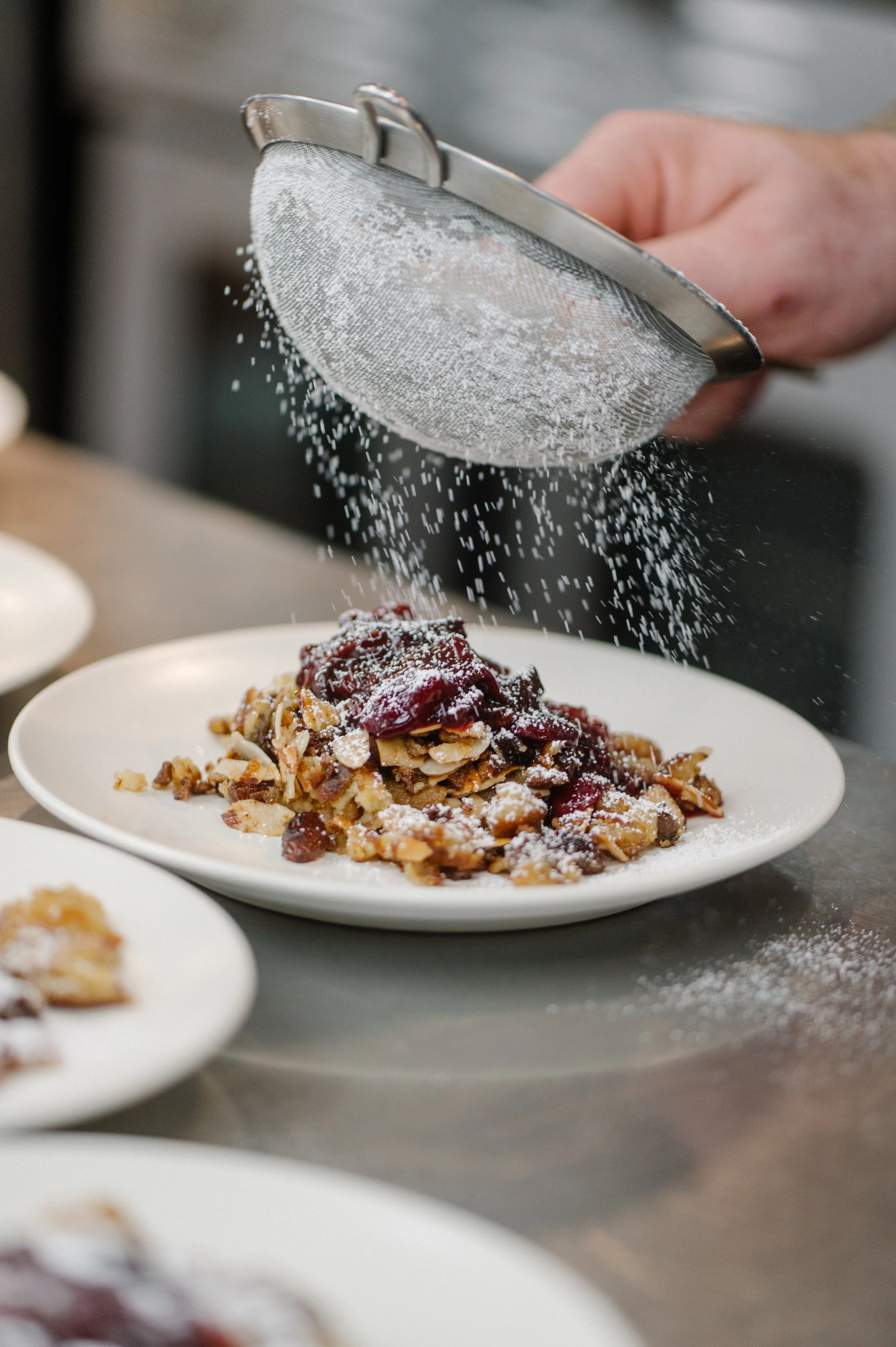 A person sifting powdered sugar over a plate of cherry dessert with nuts.