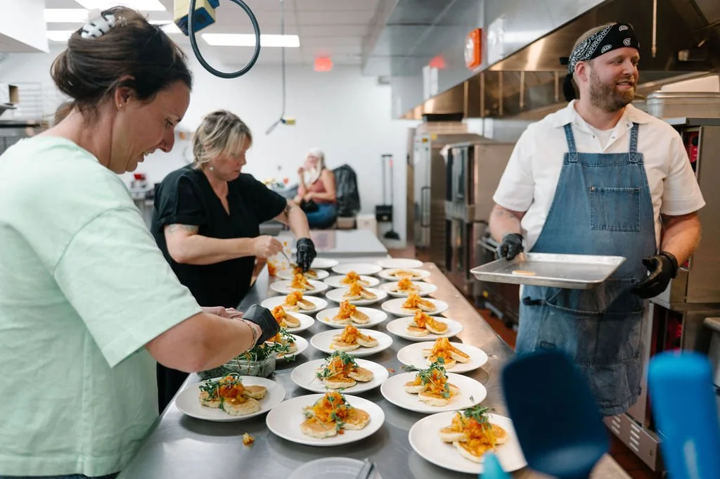 Chefs and kitchen staff preparing multiple plates of food in a commercial kitchen.