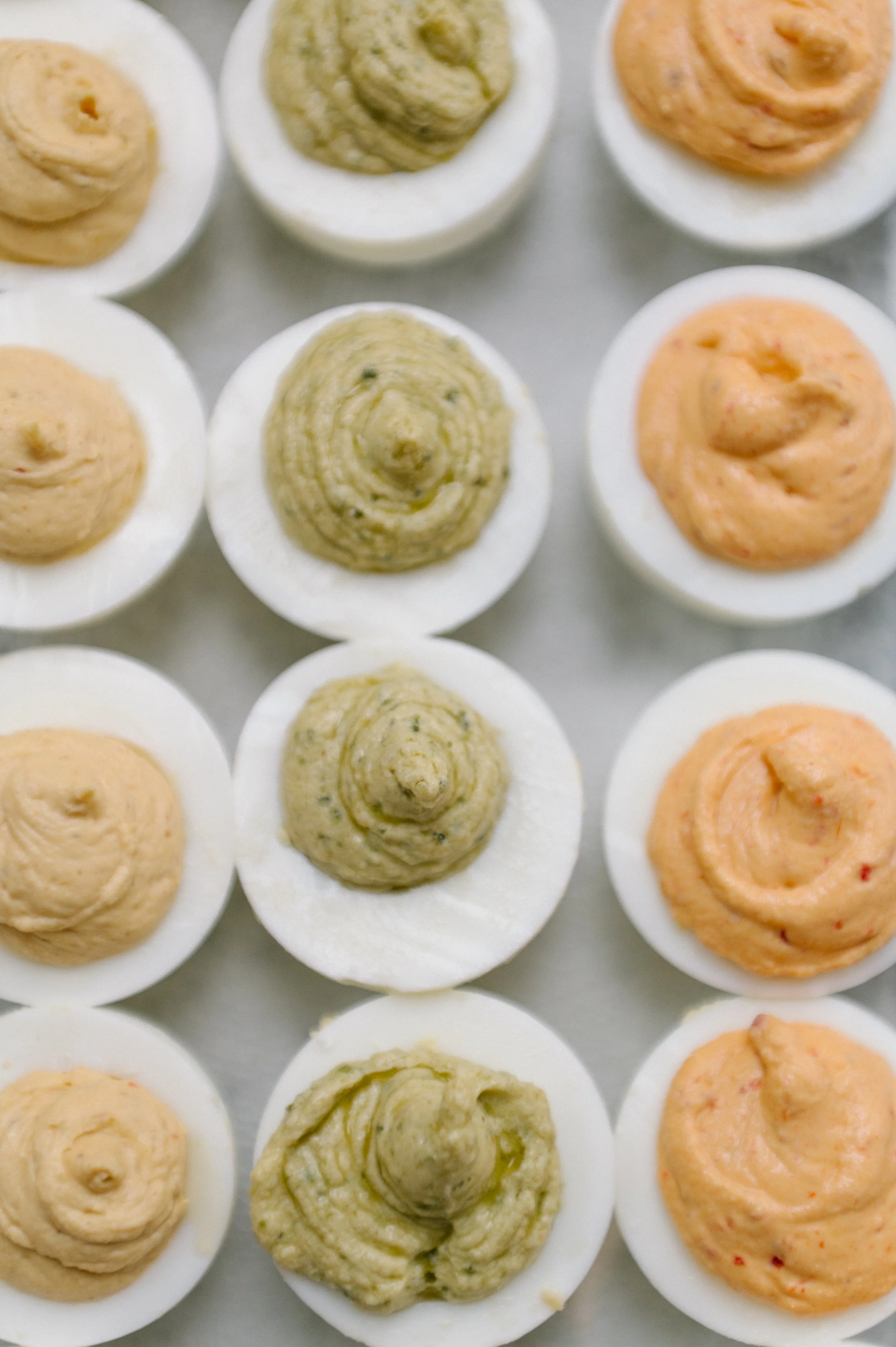 Multiple deviled eggs with different fillings, arranged on a white surface.