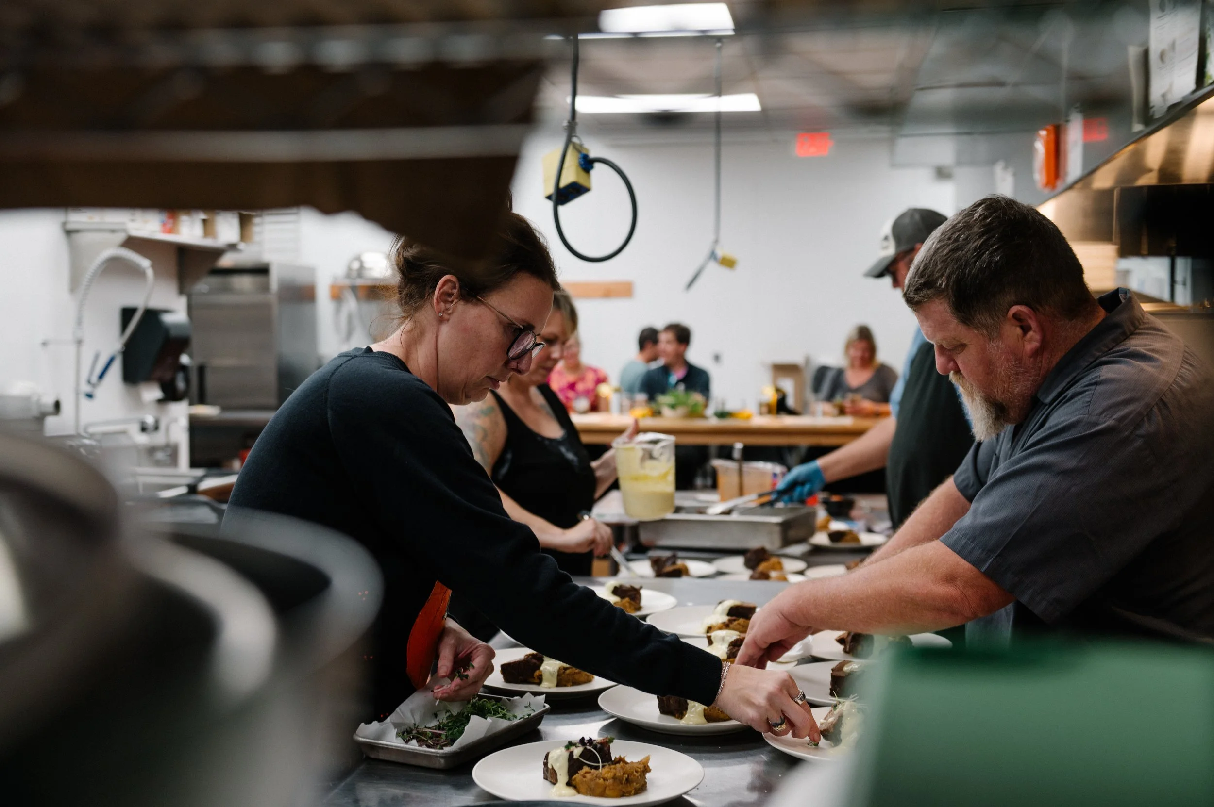 Chefs and kitchen staff preparing plated dishes in a busy restaurant kitchen.