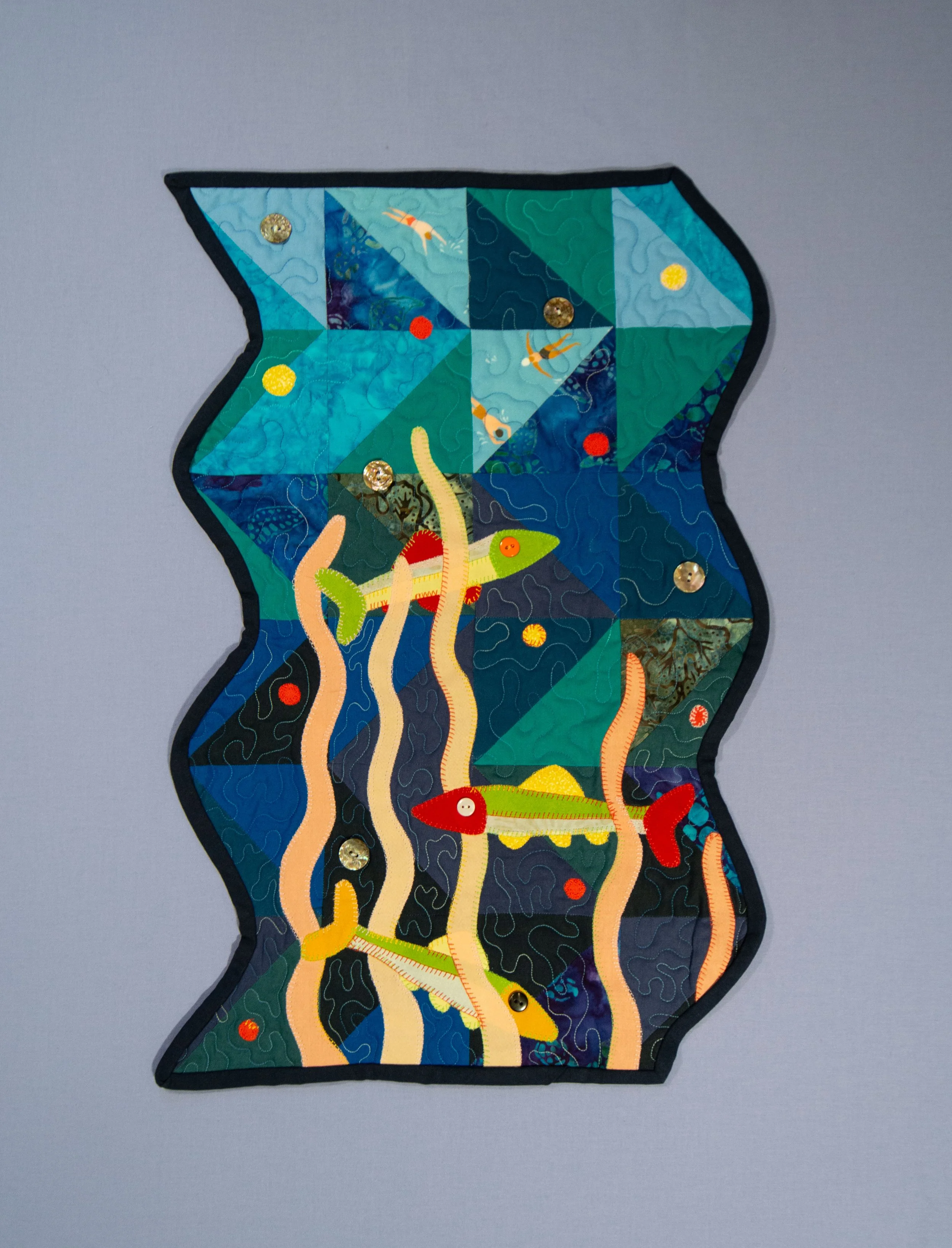 Applique fish and aquatic plants on a patchwork background art quilt.