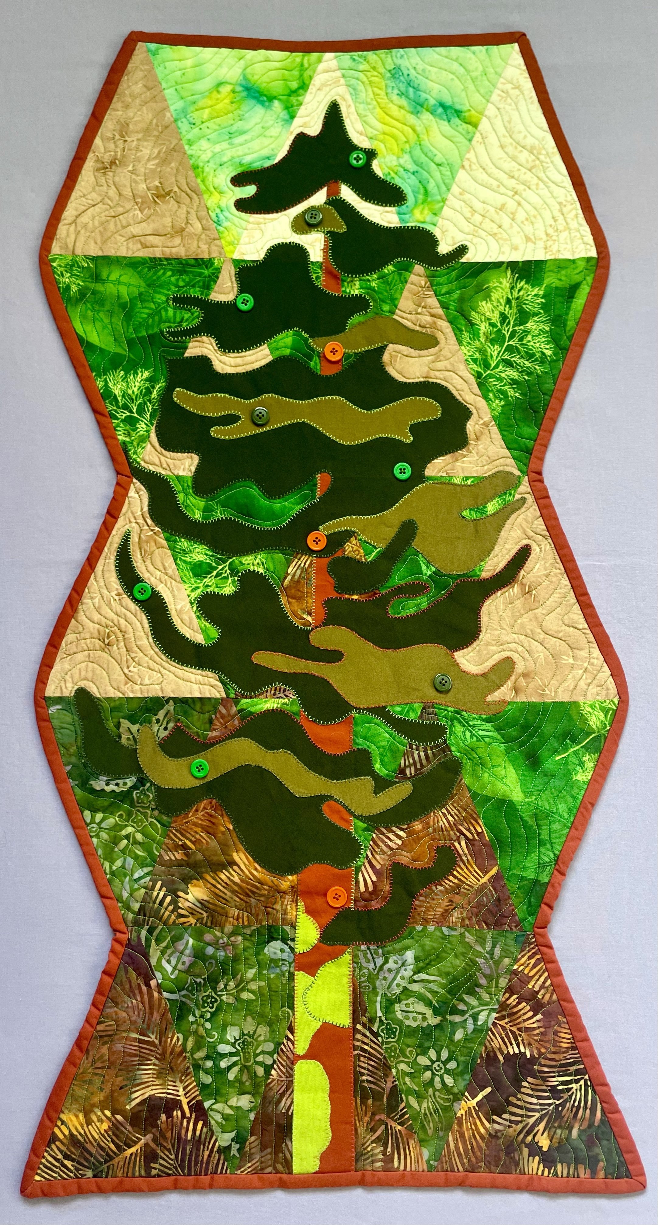A quilted wall hanging featuring a rainforest scene with a tall, flowering plant with large leaves, in earthy tones of green, brown, and beige, accented with bright orange and green buttons, bordered with an orange trim.