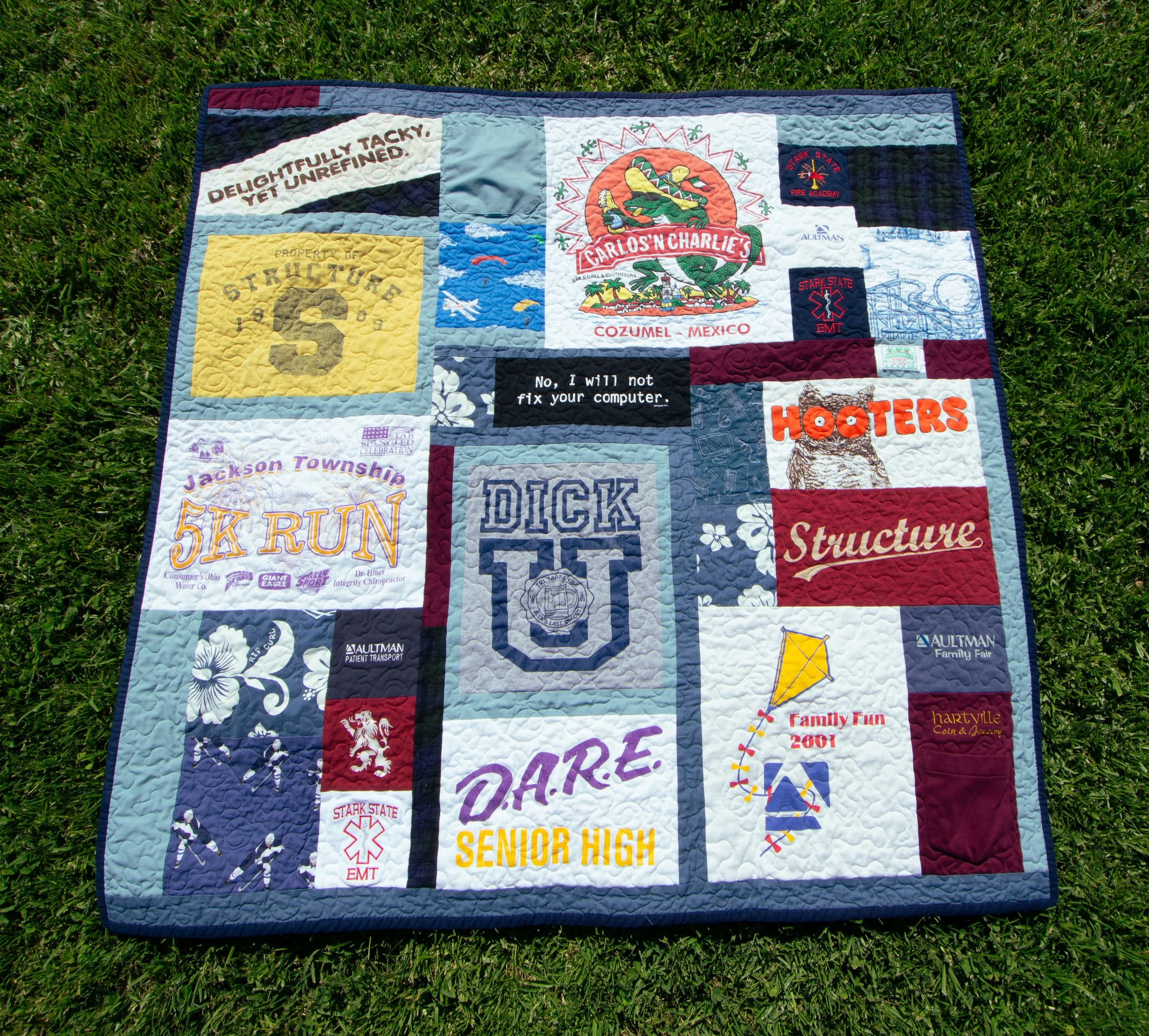 A memorial quilt on green grass with various tshirts arranged.