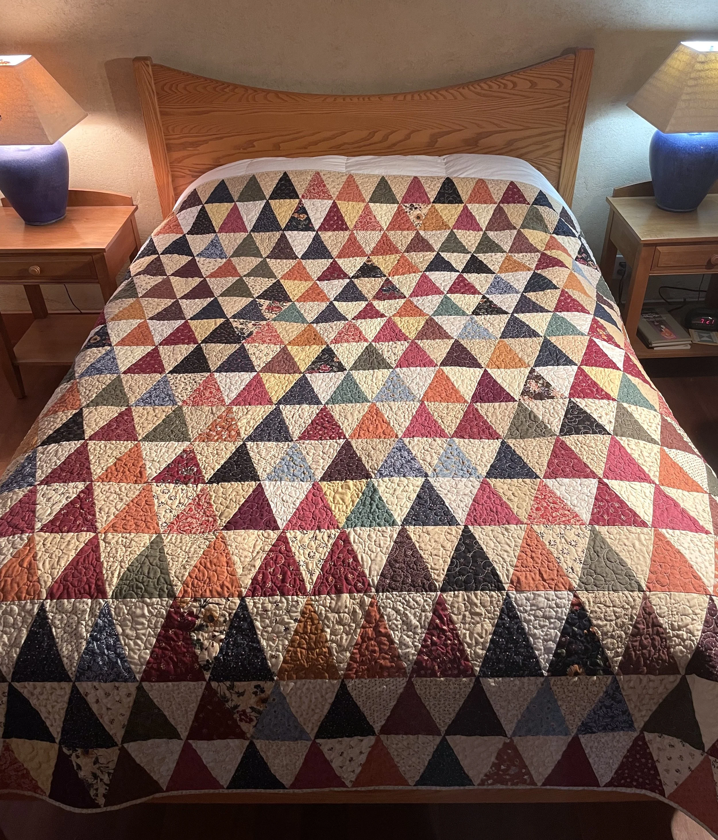 Quilt on a bed with repeated triangles in muted color palette.