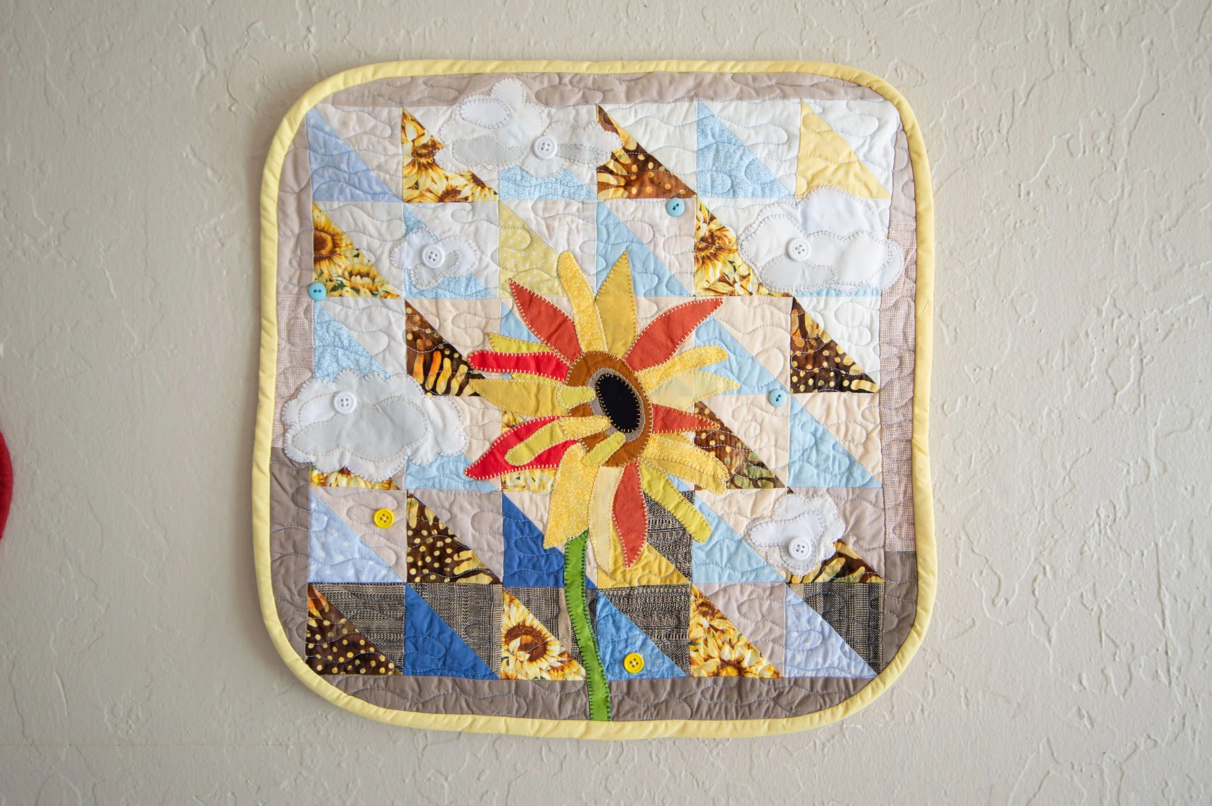 Applique A small sunflower art quilt in yellows, oranges and blues on a plain background