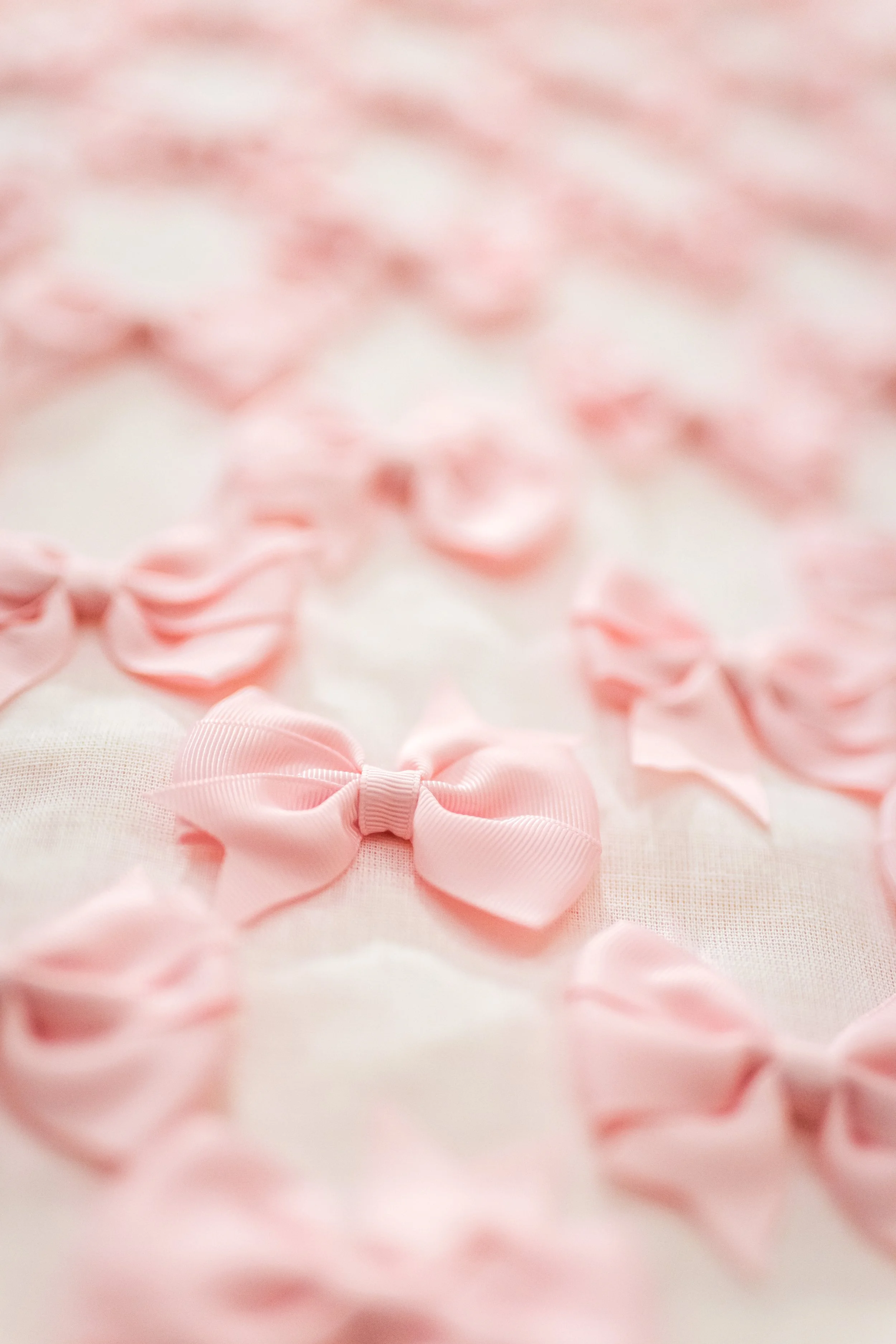 A pink fabric background with several pink ribbons and bows in the foreground.