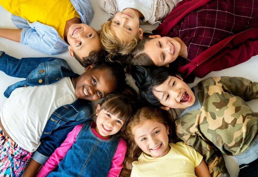 Group of smiling children lying in a circle together, reflecting friendship, belonging and a welcoming school community.