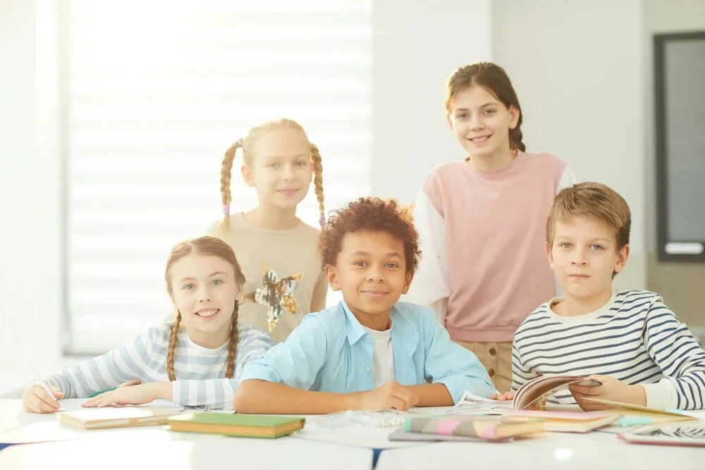 Five smiling students gathered around a classroom table, reflecting friendship, confidence and a welcoming school community.